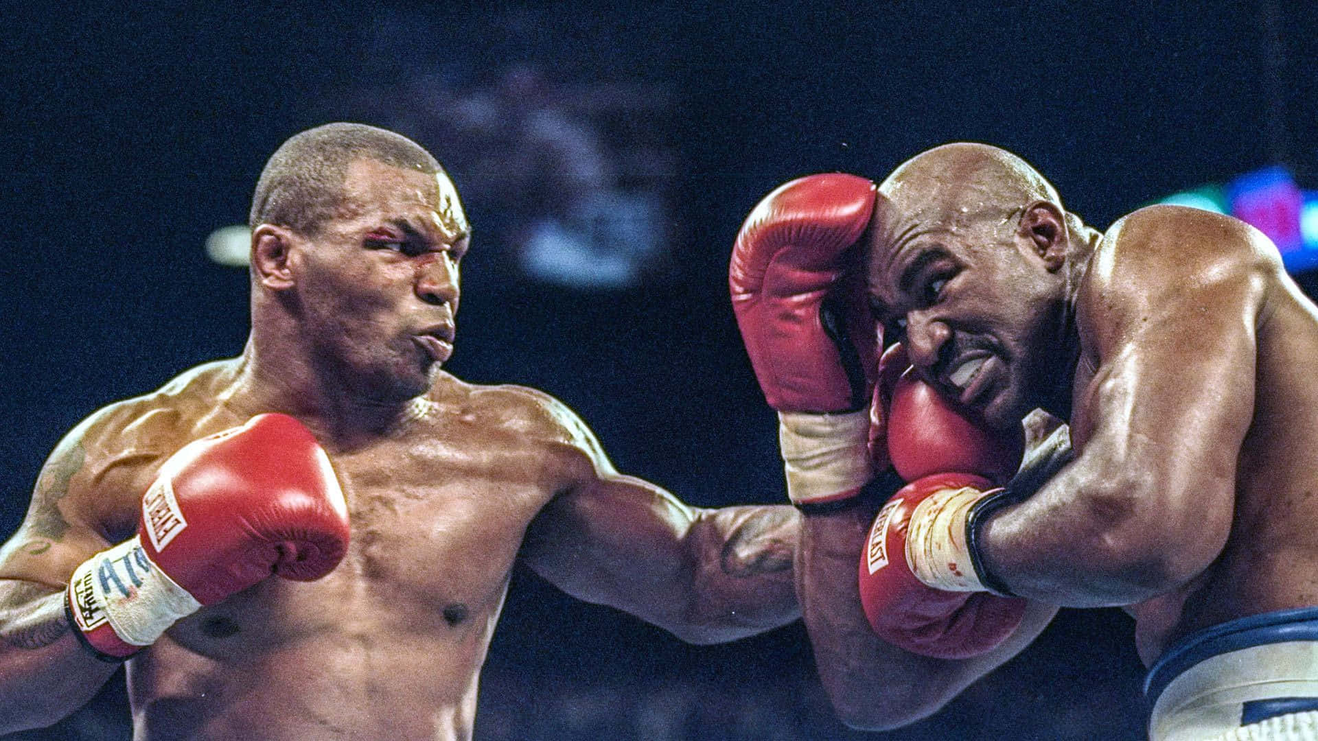 mike tyson 桌布 壁紙 — 兩名肌肉發達的拳擊手在擂台上激烈交鋒，紅色手套和汗水在明亮燈光下閃閃發光。