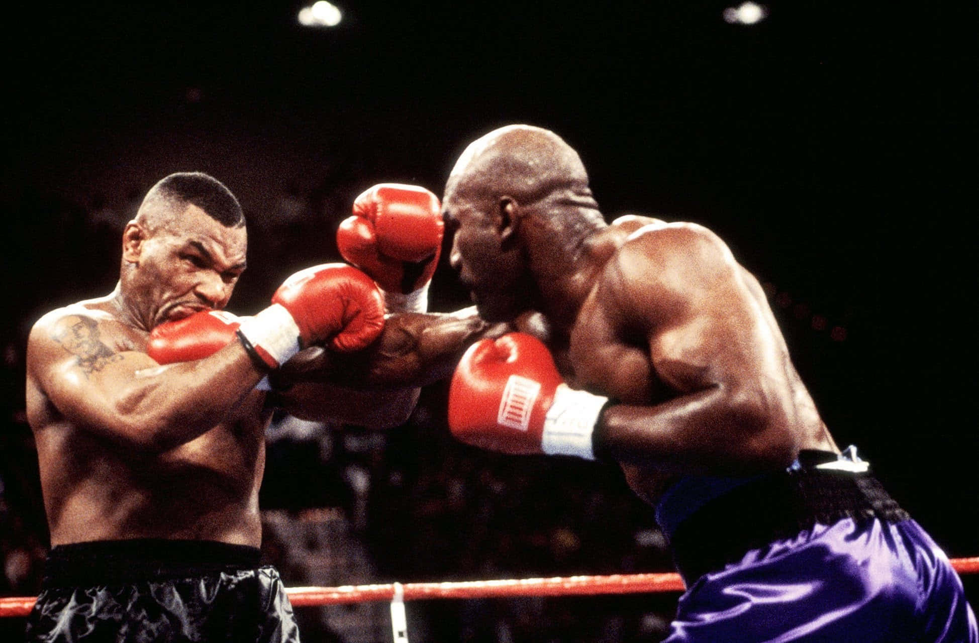 mike tyson 桌布 壁紙 — 兩名肌肉發達的拳擊手在燈光璀璨的擂台上，戴著紅色手套，以專注的強度激烈交鋒。
