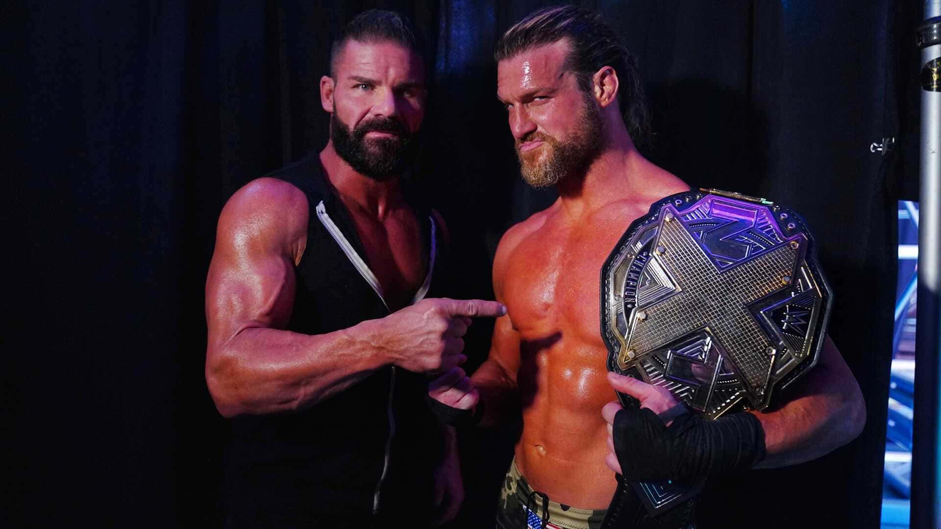 Dolph Ziggler Mason Ryan 壁紙 — 兩名肌肉發達的摔角手擺出強烈姿勢，一人手持冠軍腰帶並指向另一人，背景為深色。