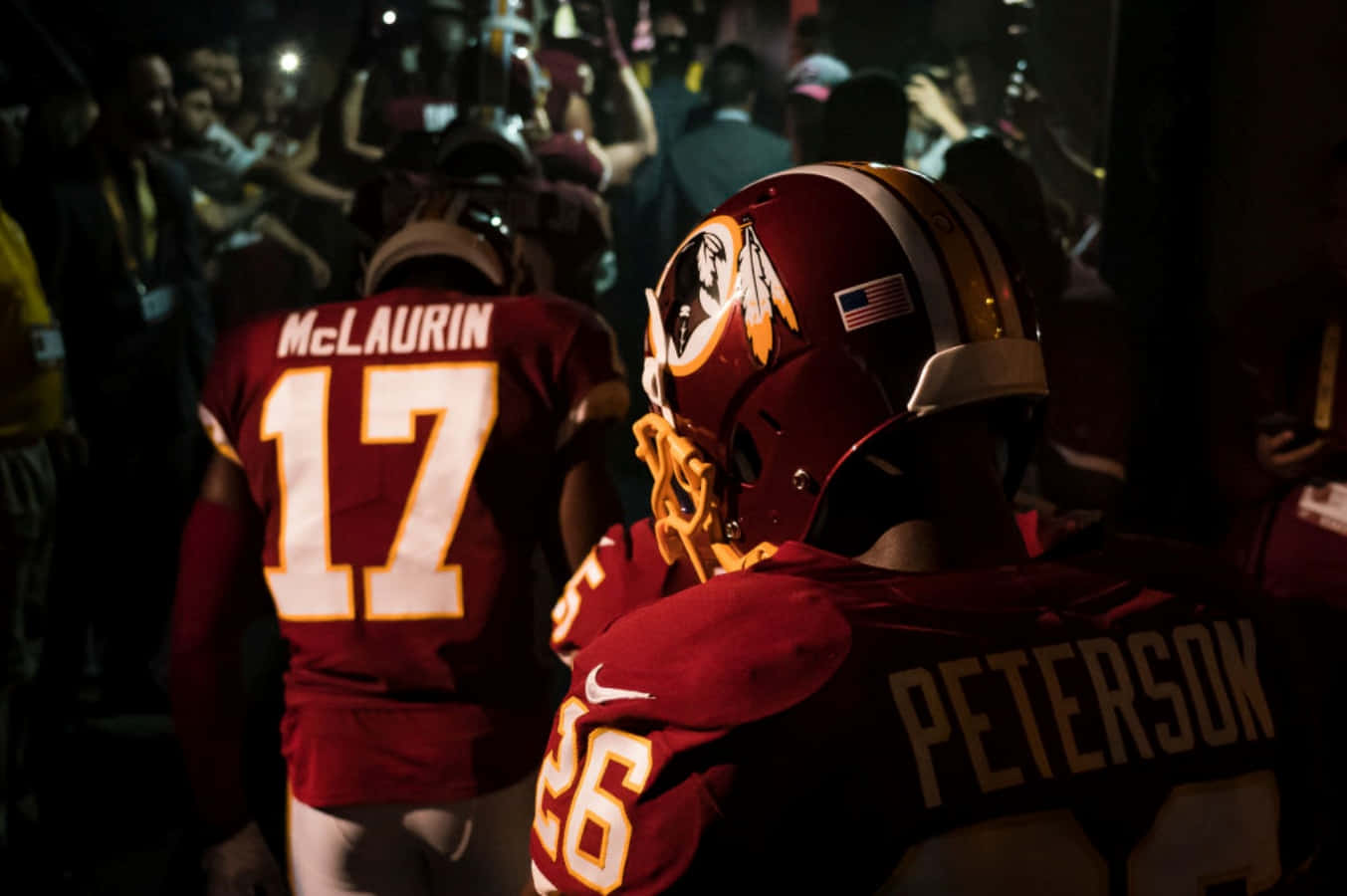 Washington Football 桌布 壁紙 — 兩名華盛頓美式足球隊球員身穿栗色球衣，穿過燈光昏暗的隧道，身後有球迷歡呼。