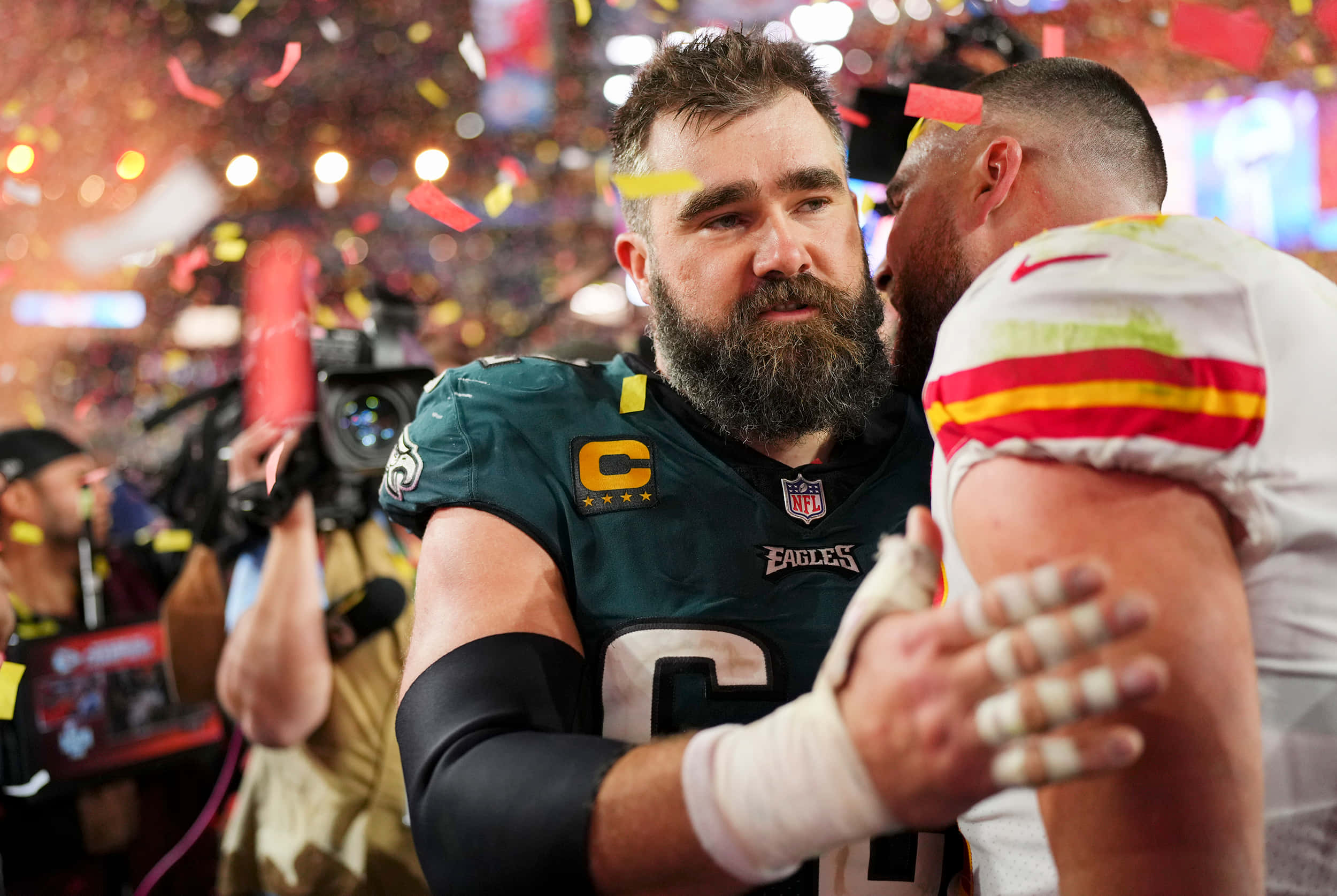 Jason Kelce 桌布 壁紙 — 兩名足球運動員在冠軍勝利後，在飄落的五彩紙屑和體育場燈光中擁抱。
