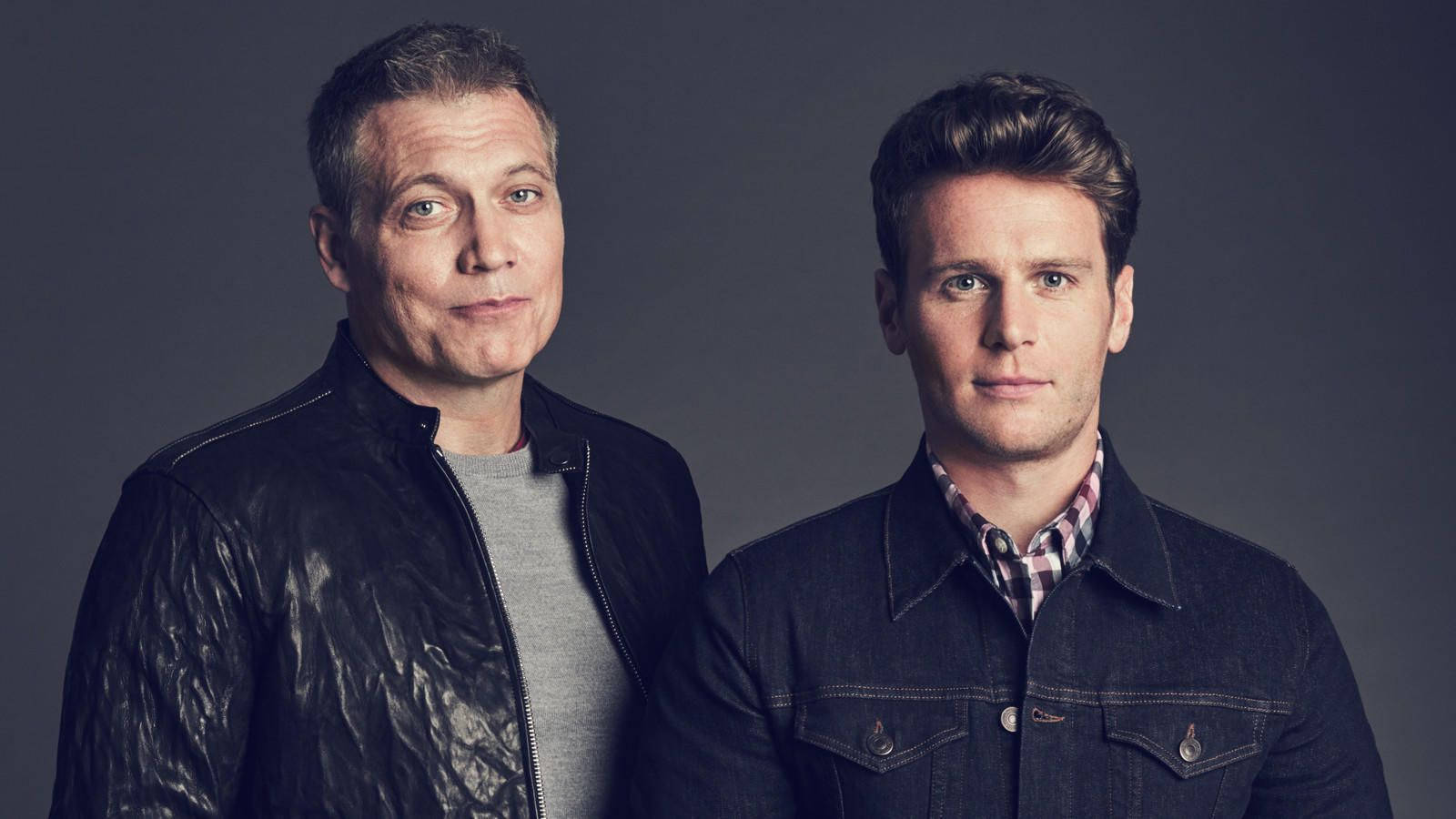 Netflix Mindhunter Power Duo 壁紙 — 兩名身穿外套的男子在深灰色攝影棚背景前，以柔和燈光嚴肅地擺姿勢。