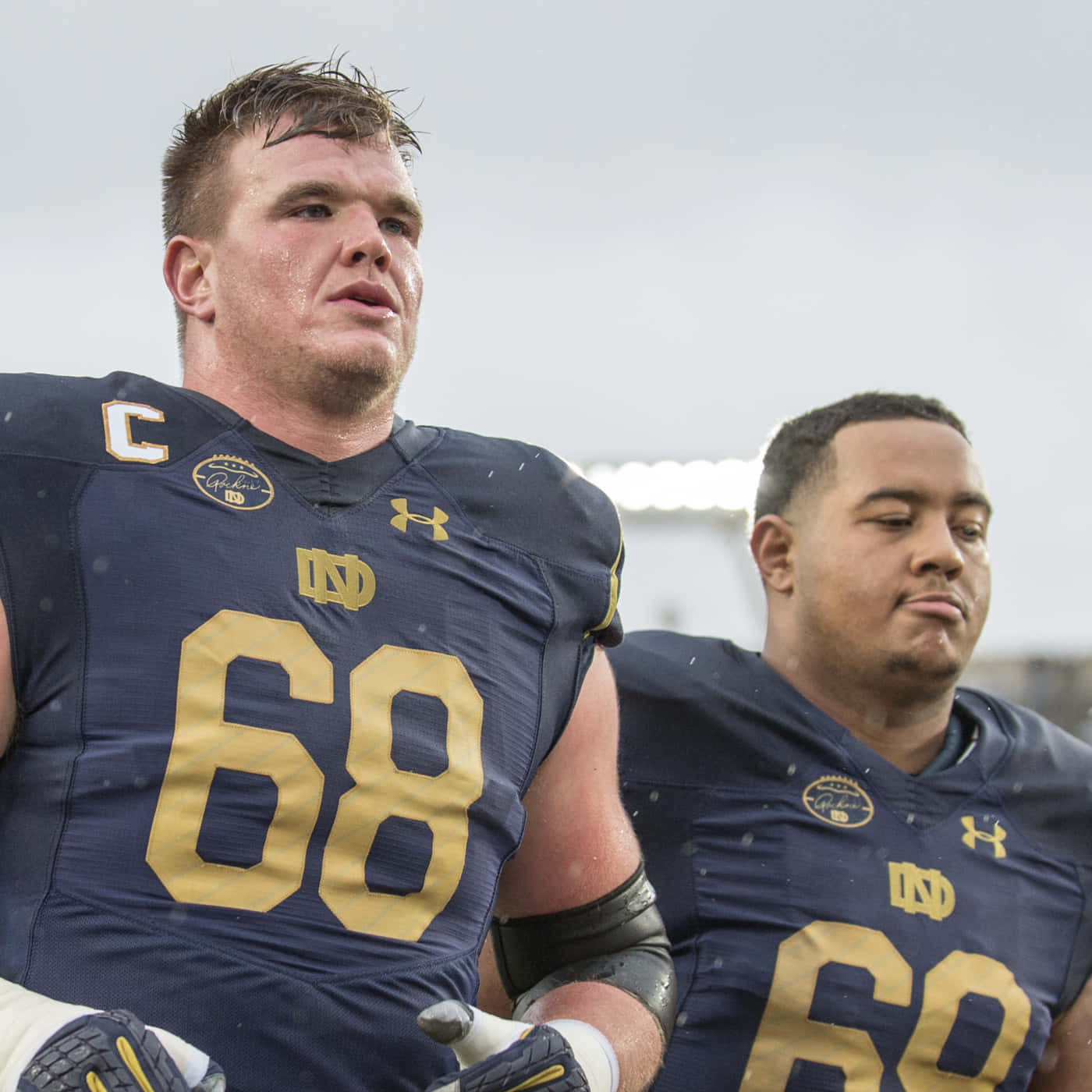 Mike Mcglinchey 桌布 壁紙 — 兩名身穿海軍藍和金色球衣、汗流浹背的足球運動員站在陰天下的雨地球場上。