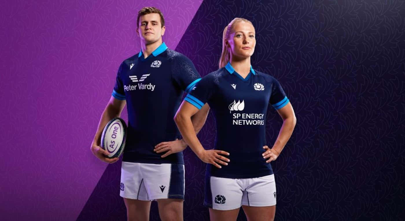 Scotland Rugby 桌布 壁紙 — 兩名身穿海軍藍球衣的欖球運動員在紫色圖案背景前自信地擺姿勢，其中一人手持欖球。