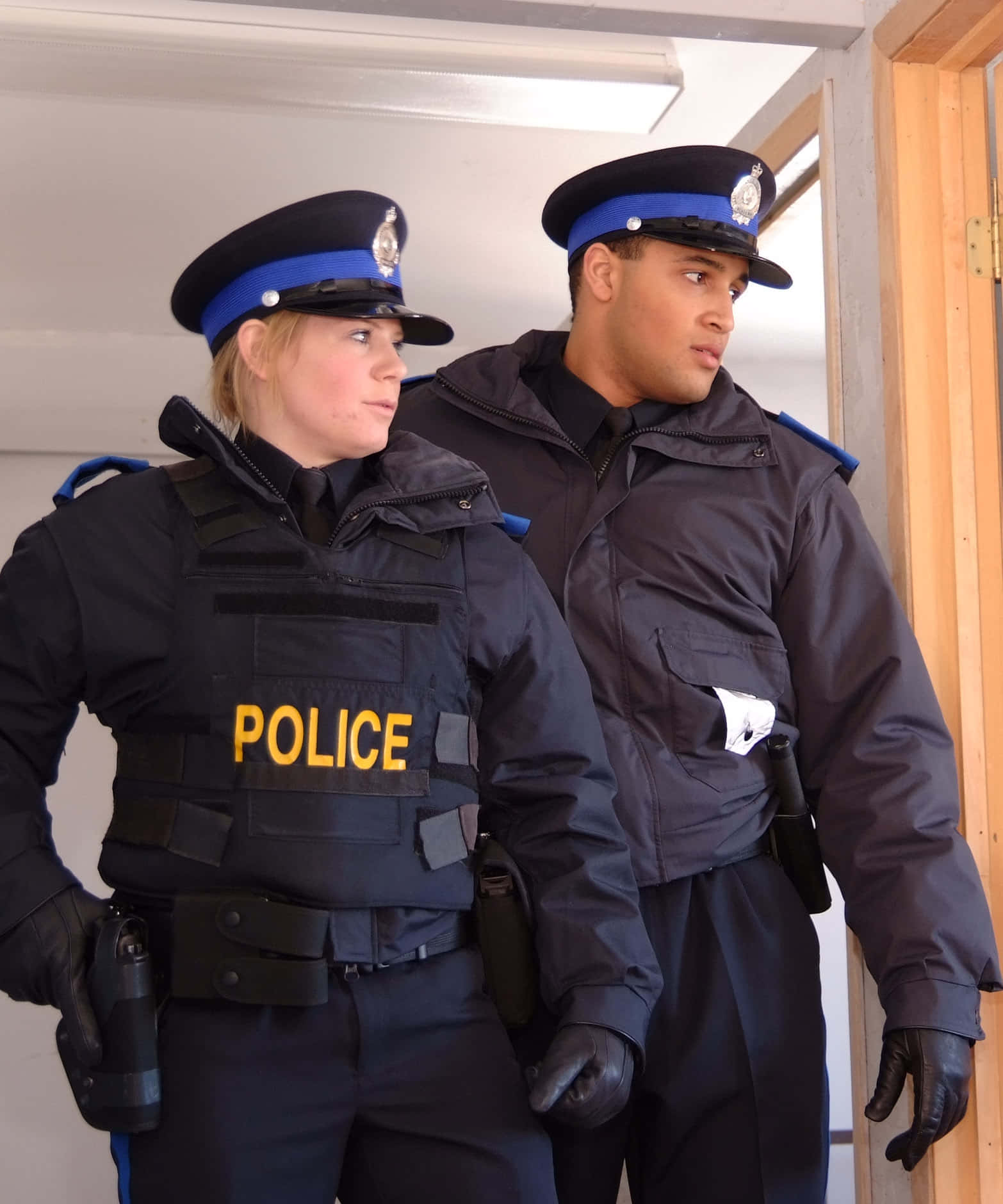 警察 桌布 壁紙 — 兩名身穿深色制服嘅警察喺室內警覺咁企喺度，表情嚴肅。