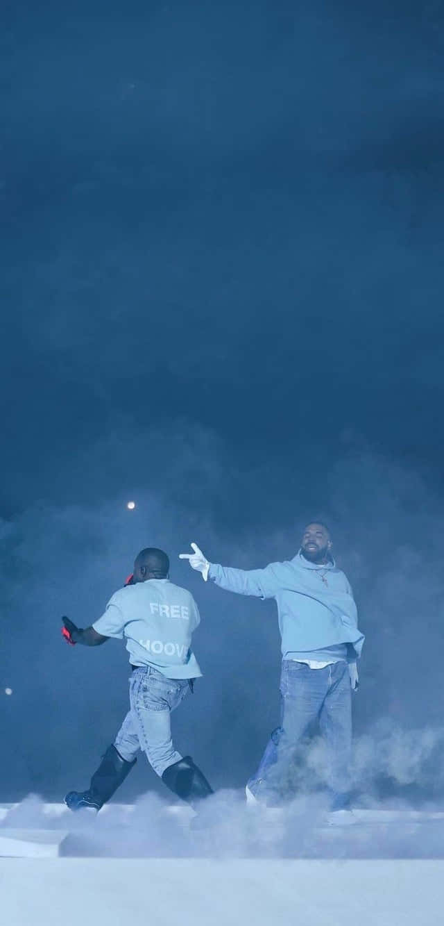 Drake 桌布 壁紙 — 兩名身穿淺藍色連帽衫的男子在昏暗的舞台燈光下，穿過濃厚的藍色煙霧，做出充滿動感的手勢。