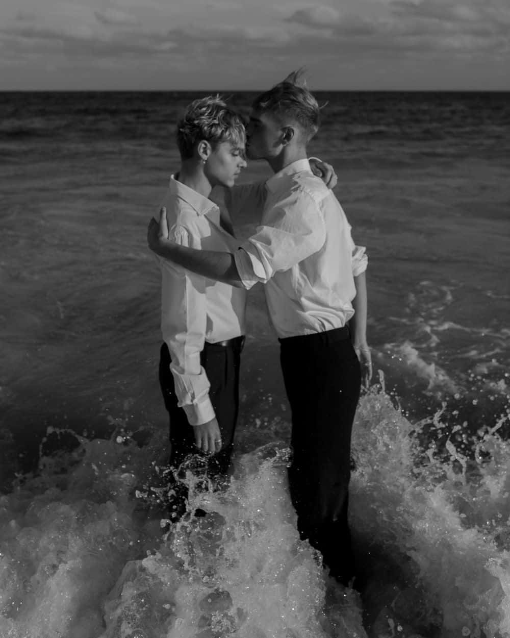 Lovers 桌布 壁紙 — 兩名身穿白恤衫的男子在黃昏的海浪中溫柔相擁，黑白照片。