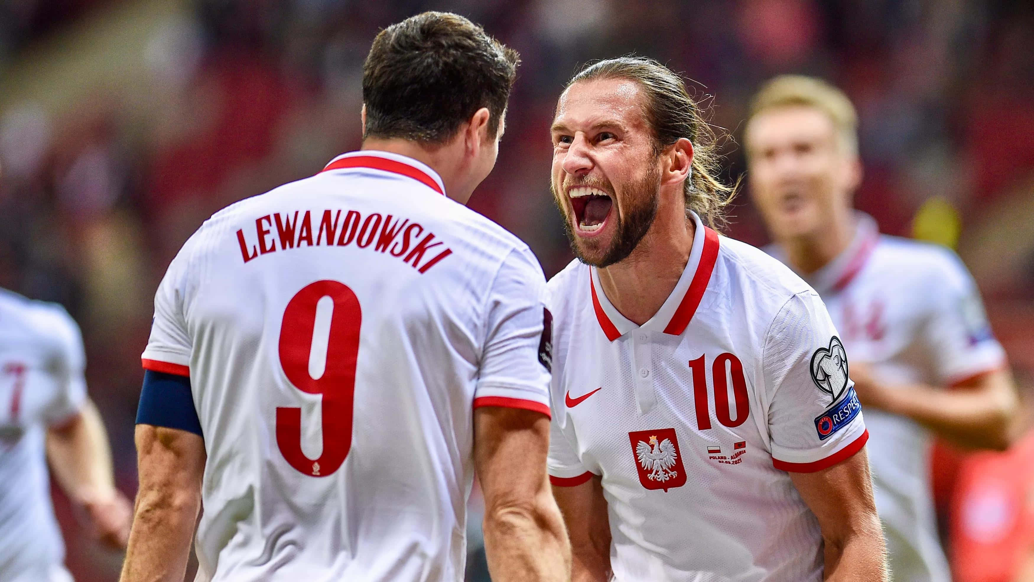 Poland 桌布 壁紙 — 兩名身穿白色球衣的波蘭足球運動員在球場上熱情慶祝，背景是模糊的球迷。