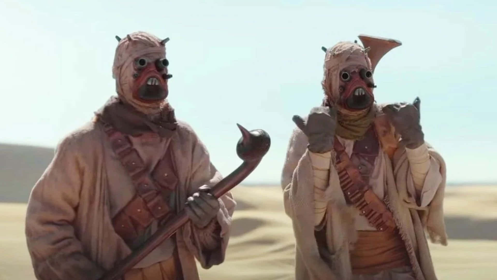 Tusken Raiders 桌布 壁紙 — 兩名身穿米色長袍、居住於沙漠的外星戰士，站在陽光炙烤的沙丘地帶，手持武器。