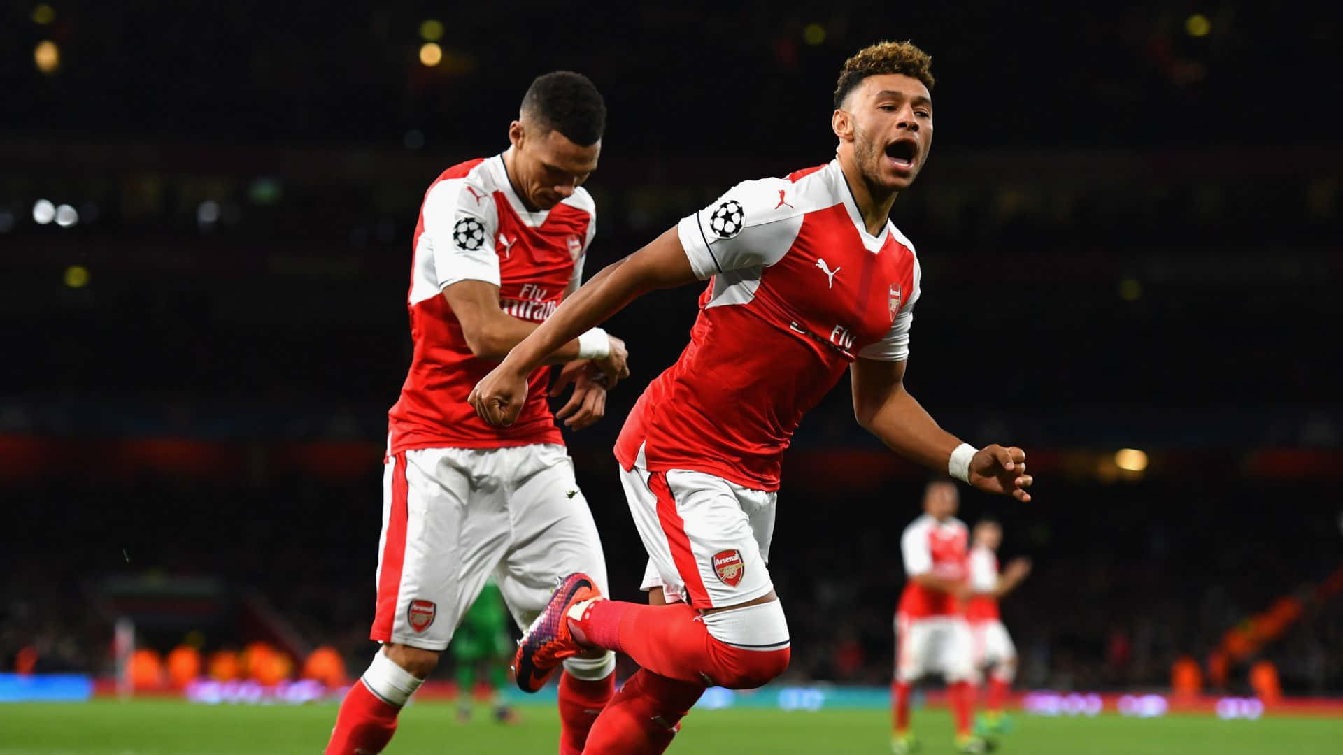 Arsenal 桌布 壁紙 — 兩名身穿紅白球衣的阿仙奴足球員在球場燈光下以強烈情感慶祝入球。