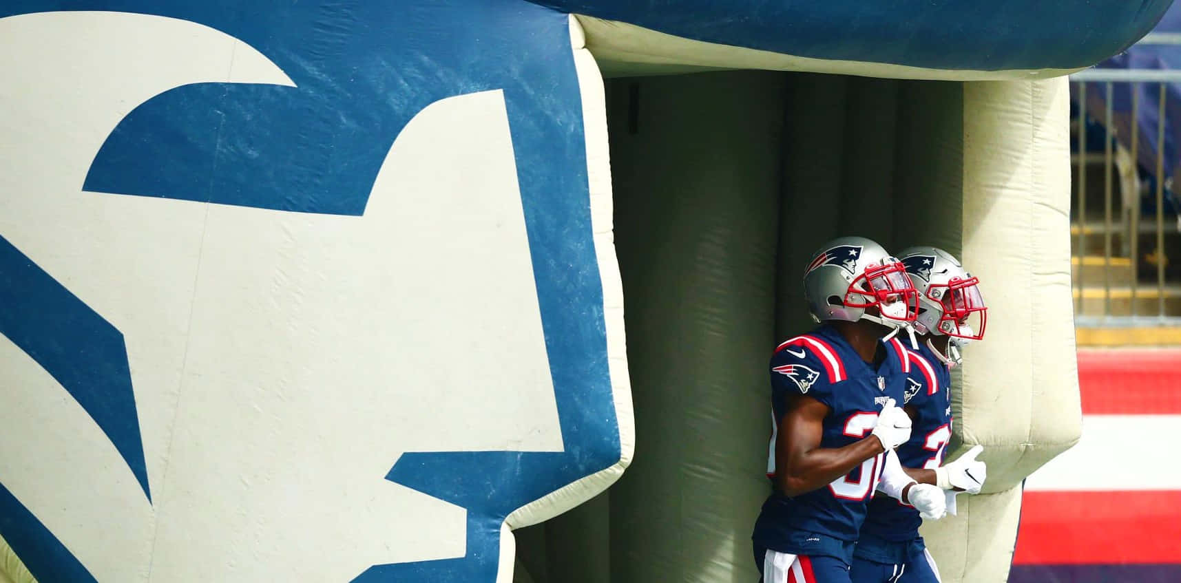 Devin Mccourty 桌布 壁紙 — 兩名身穿藍色和銀色裝備的新英格蘭愛國者隊美式足球員，在一個巨大的充氣球隊標誌旁邊穿過隧道。