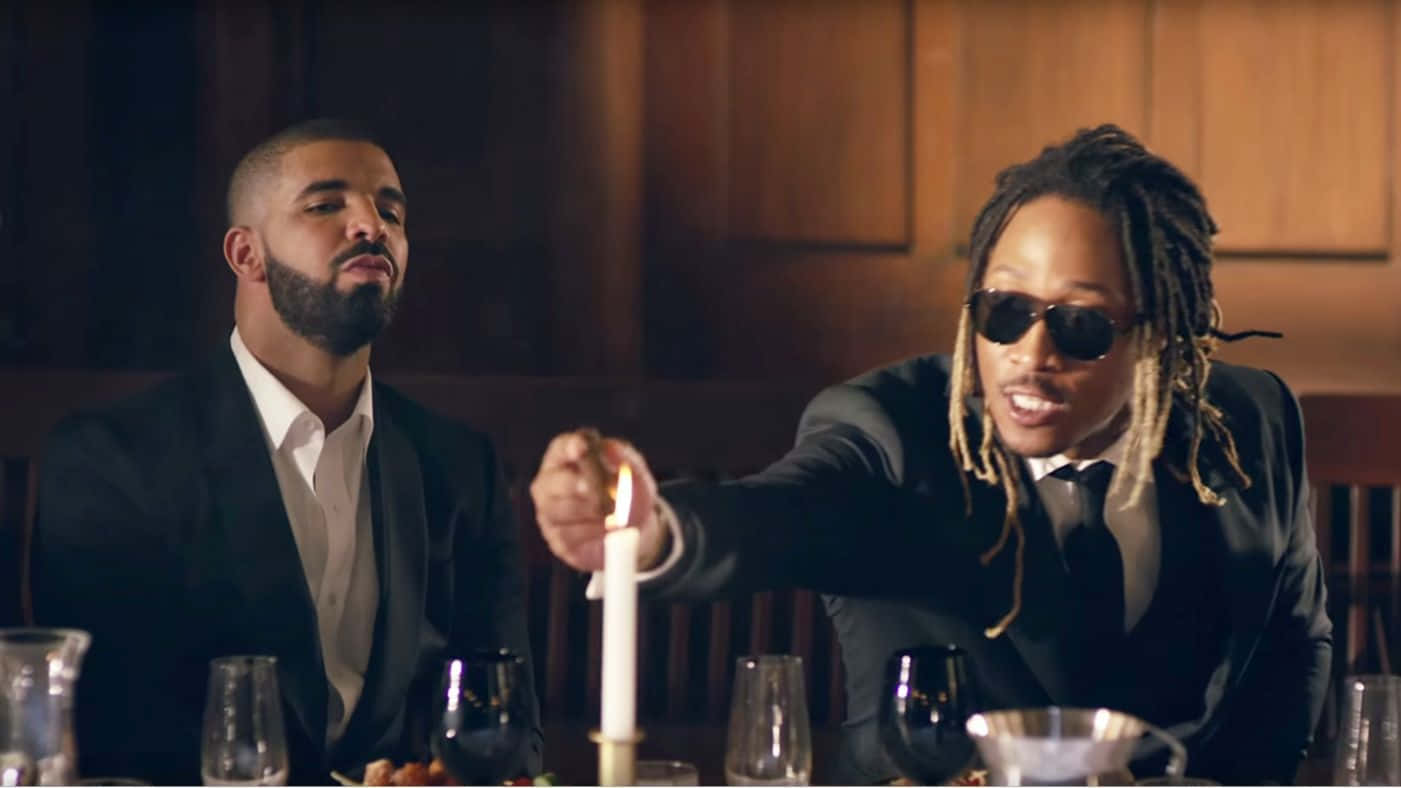 Drake 桌布 壁紙 — 兩名身穿西裝的男子坐在燭光晚餐桌旁，一人點燃蠟燭，另一人在昏暗的木鑲板房間裡觀看。