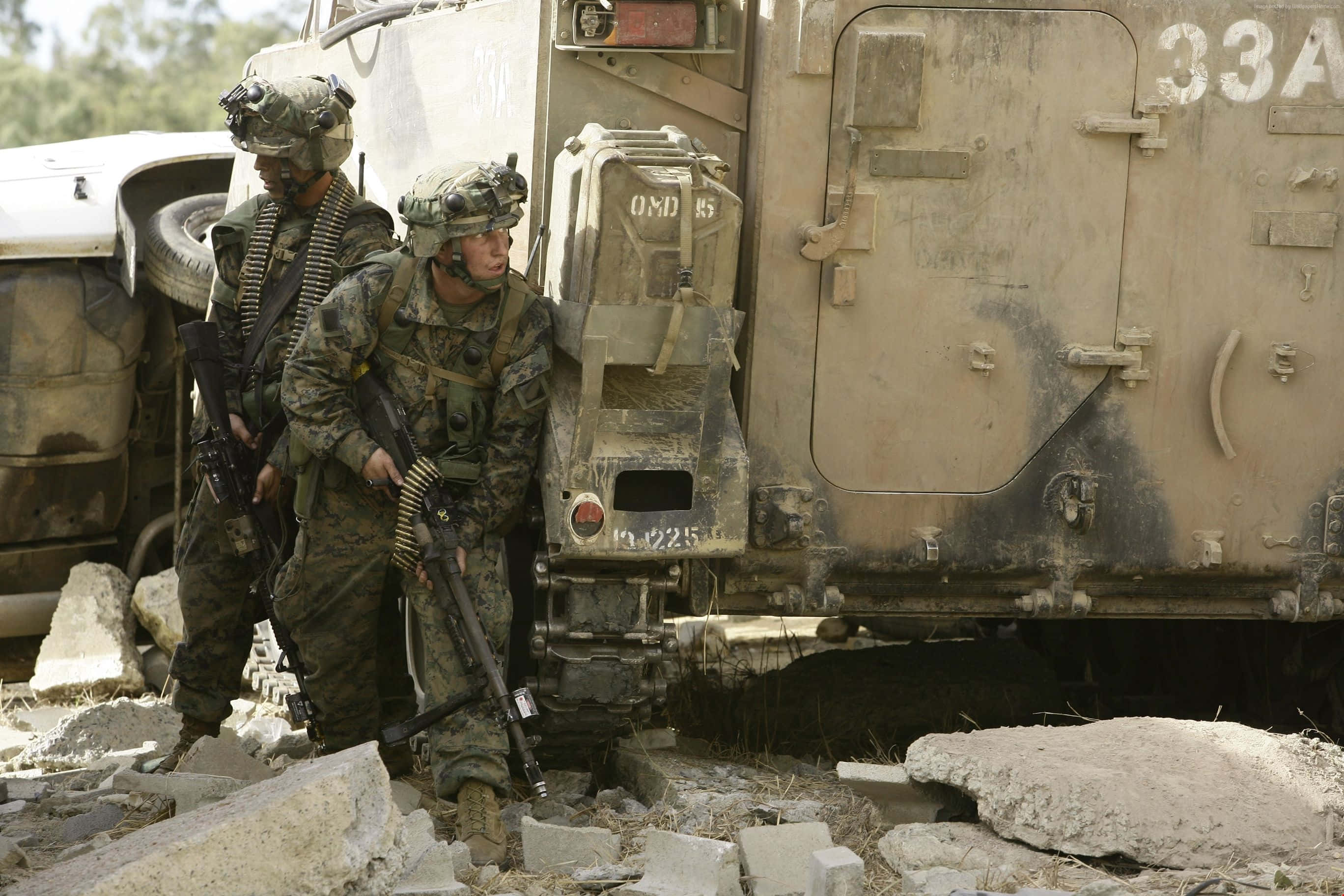 Army 桌布 壁紙 — 兩名身穿迷彩裝備的士兵站在一輛佈滿灰塵的軍用卡車旁，周圍是瓦礫，在明亮的日光下。