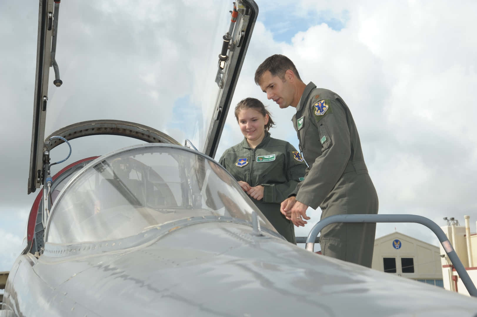 Air Force 桌布 壁紙 — 兩名身穿飛行服的機師在多雲的天空下檢查戰鬥機的駕駛艙。