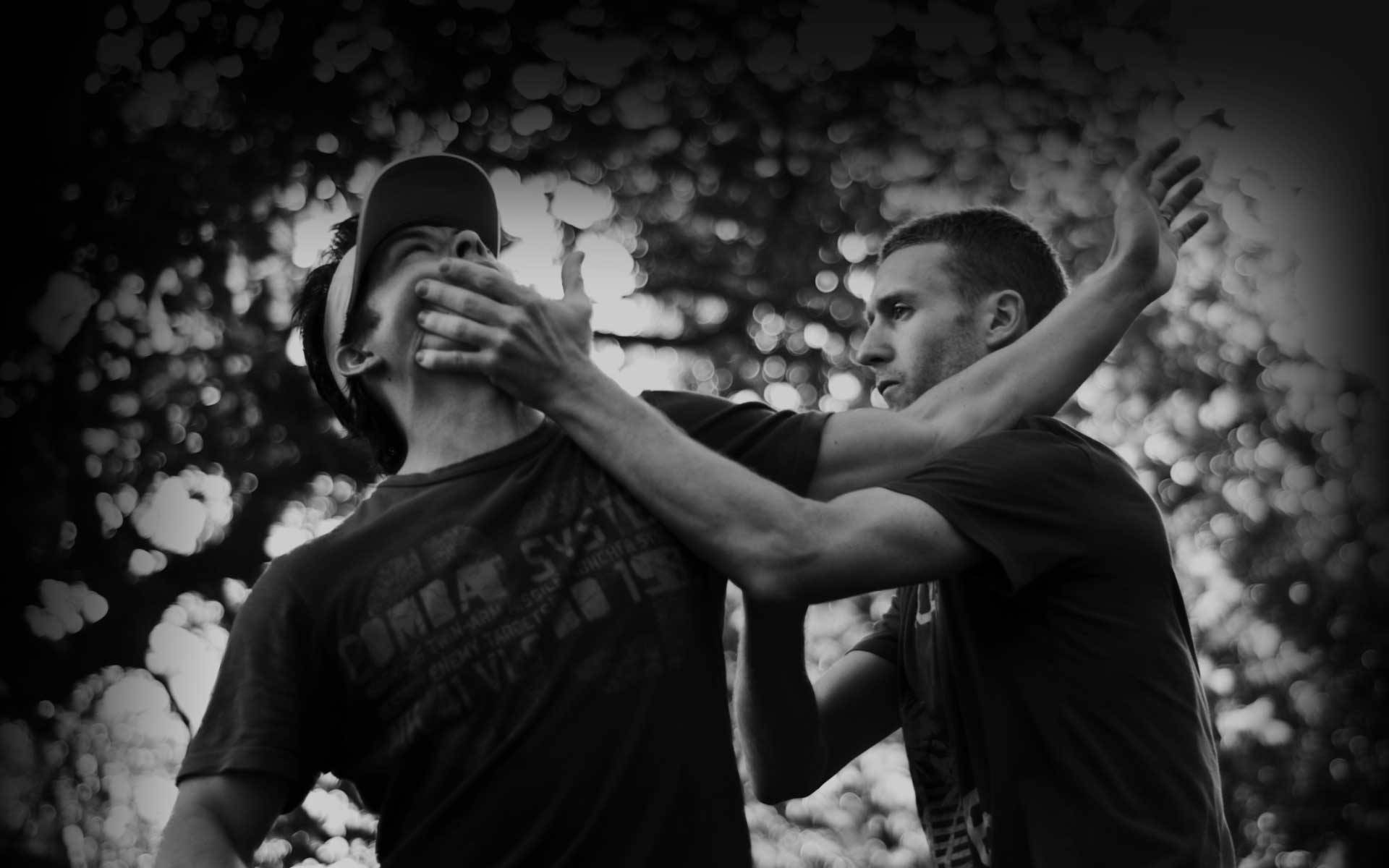 Wing Chun Fighting Art Black And White 壁紙 — 兩名身穿黑白衣服的男子在模糊的樹葉背景下進行緊張的肢體搏鬥。