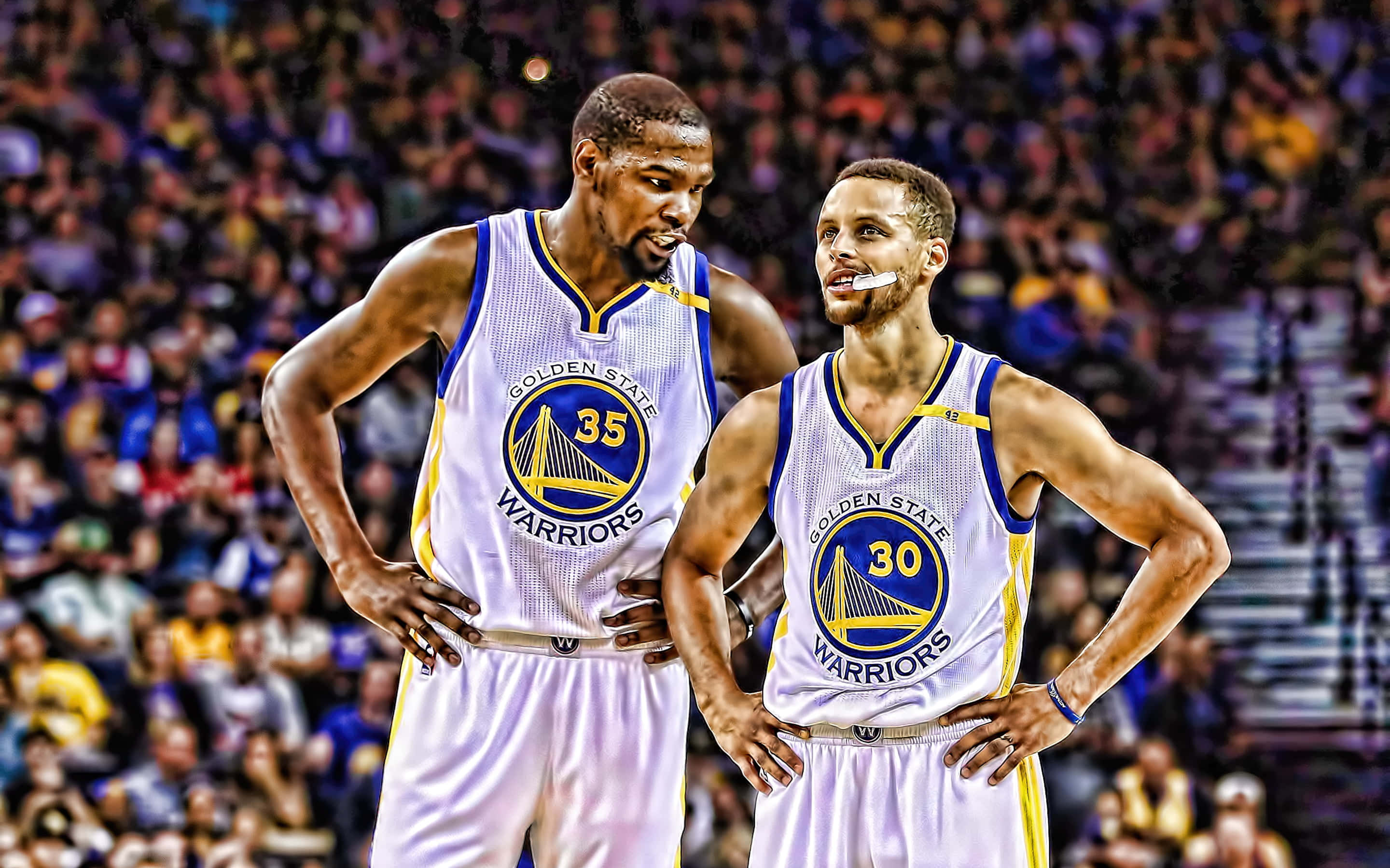steph curry 桌布 壁紙 — 兩名金州勇士隊籃球運動員在明亮的場館燈光下，雙手叉腰自信地站立於比賽中。