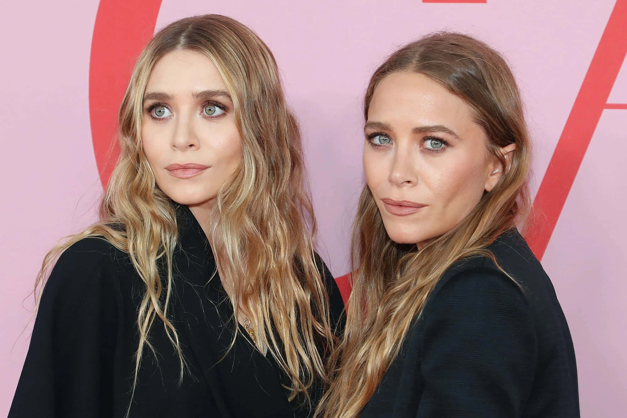 ashley olsen 桌布 壁紙 — 兩名長著長波浪金髮和引人注目的藍眼睛的雙胞胎姐妹在粉紅色和紅色的品牌背景前緊密擺姿勢。