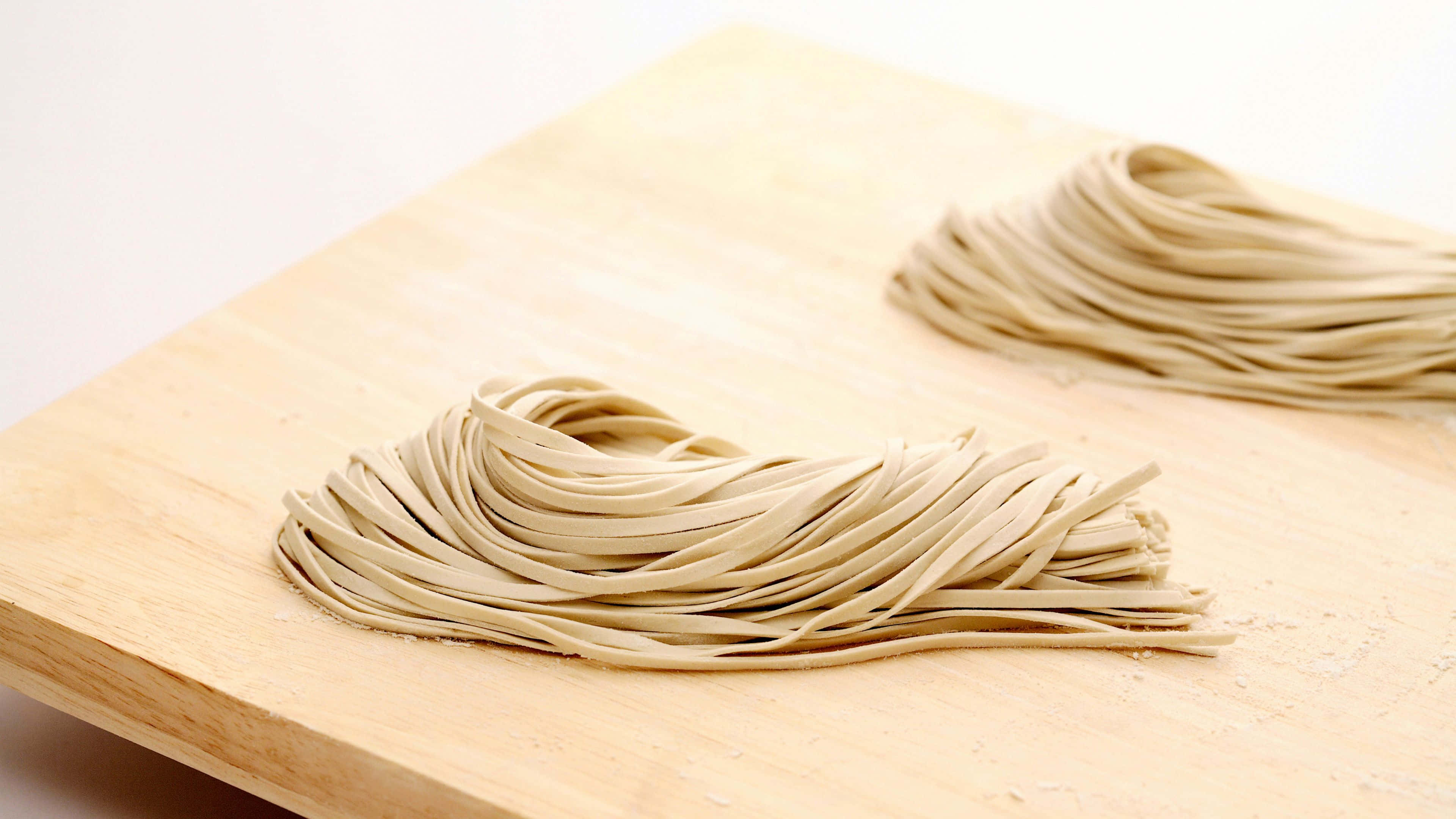 Noodles 桌布 壁紙 — 兩堆整齊的淡米色手工麵條放在灑有麵粉的淺色木砧板上。