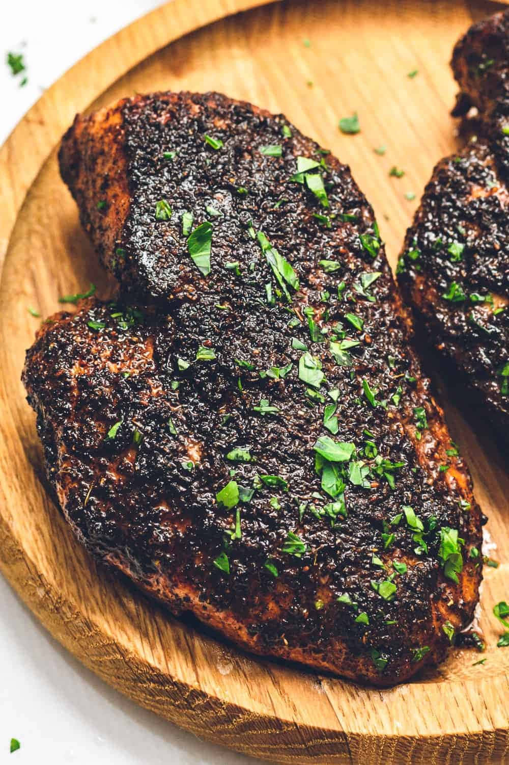 Blackened Chicken 桌布 壁紙 — 兩塊帶有深色香草外皮和新鮮歐芹的香煎雞胸肉，放在質樸的木盤上。