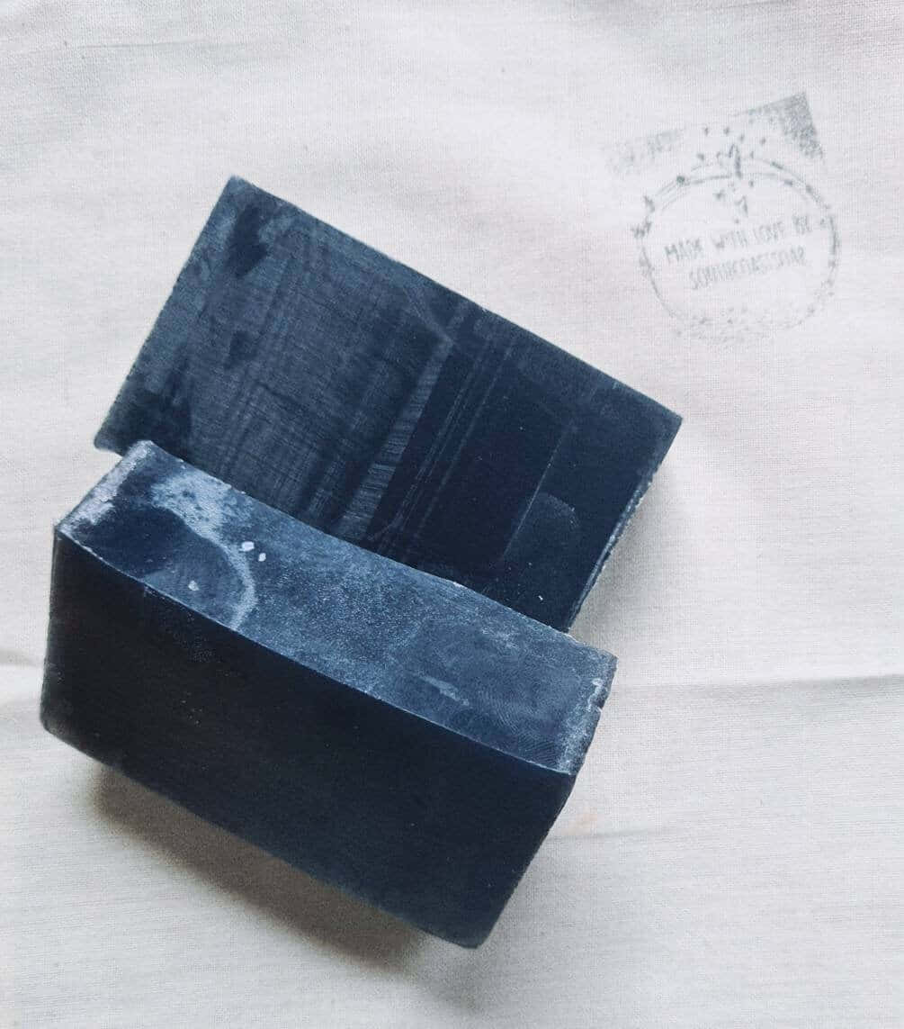 Black Soap 桌布 壁紙 — 兩塊深藍色手工皂放在一塊帶有模糊壓印訊息的白色紋理布上。
