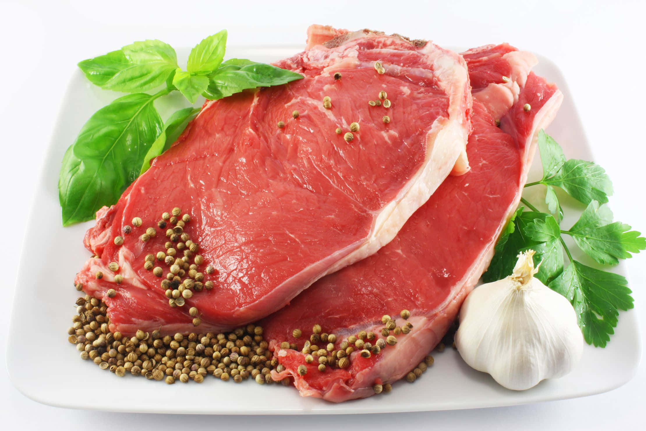 meat 桌布 壁紙 — 兩塊用胡椒粒、羅勒和大蒜調味的生牛肉扒放在白色碟子上，背景是潔淨的白色。