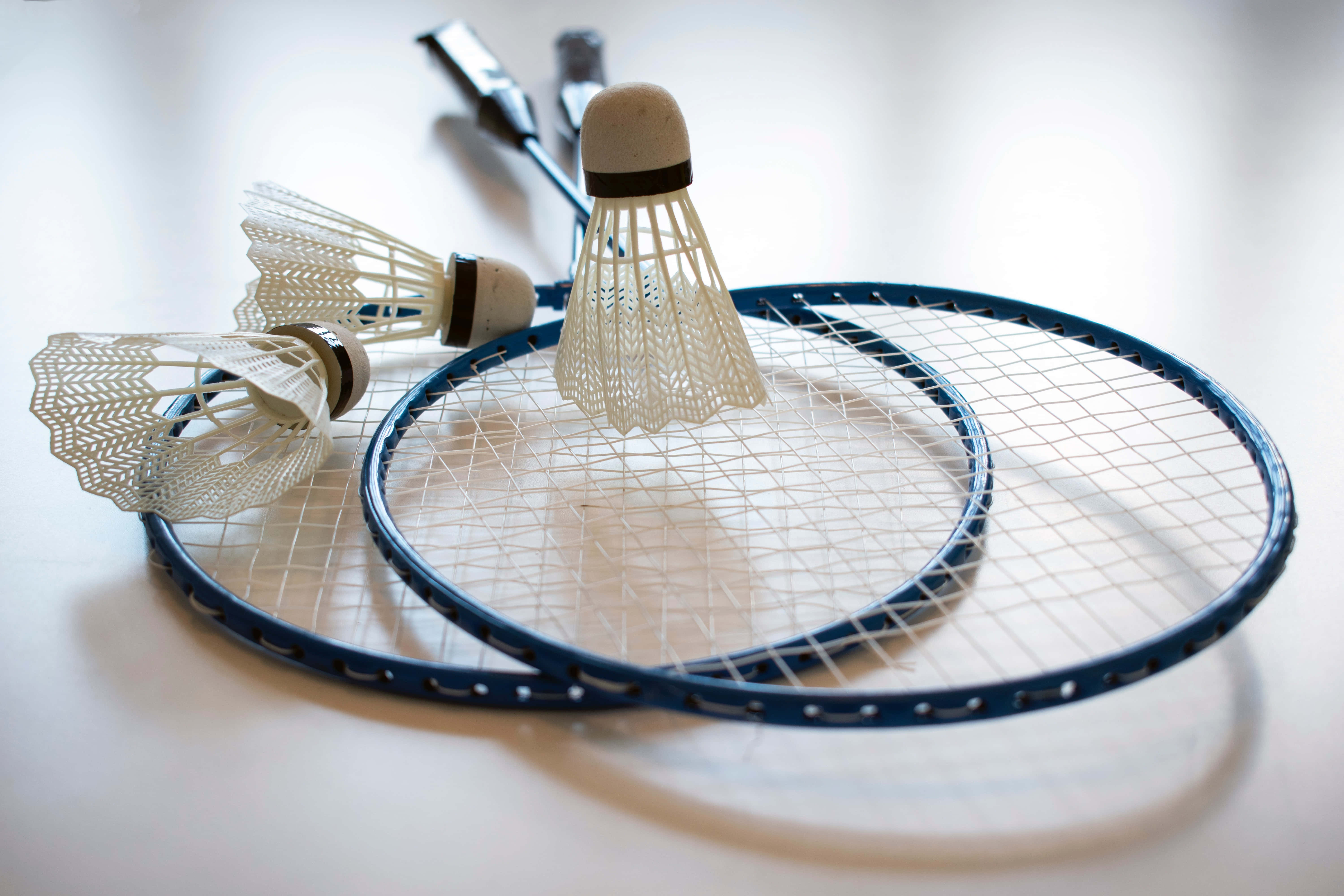 Badminton 桌布 壁紙 — 兩塊藍色羽毛球拍和三個羽毛球放在明亮的白色表面上，帶有柔和陰影。
