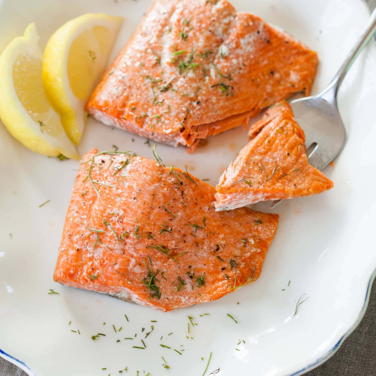 Salmon 桌布 壁紙 — 兩塊調味三文魚柳配檸檬角及蒔蘿，放在白色碟上，附有叉子。