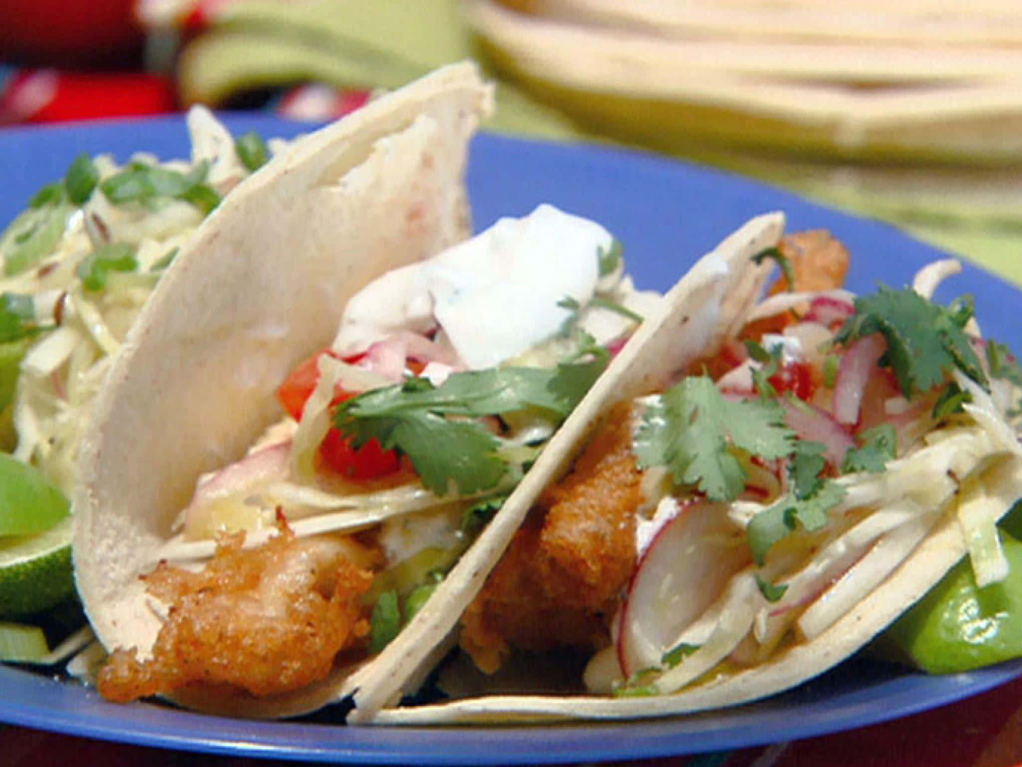 Taco 桌布 壁紙 — 兩塊香脆魚肉墨西哥卷，配上奶油醬、新鮮芫荽和蘿蔔片，放在鮮藍色的碟子上。