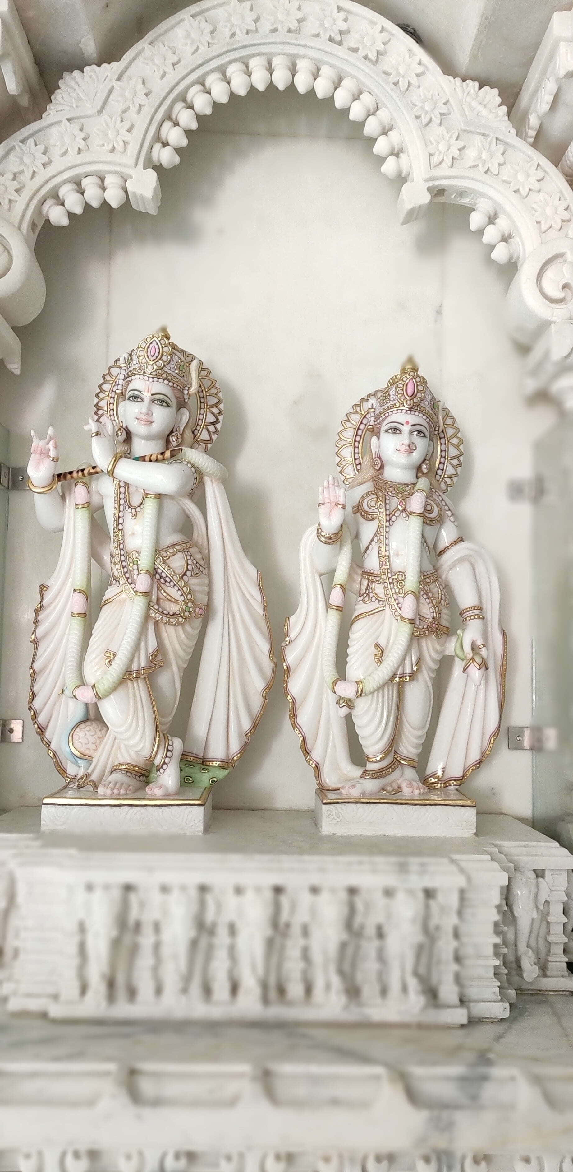 Radha Krishna 桌布 壁紙 — 兩尊精雕細琢的白色大理石印度教神像矗立在寺廟中一個細節豐富的拱形壁龕下。