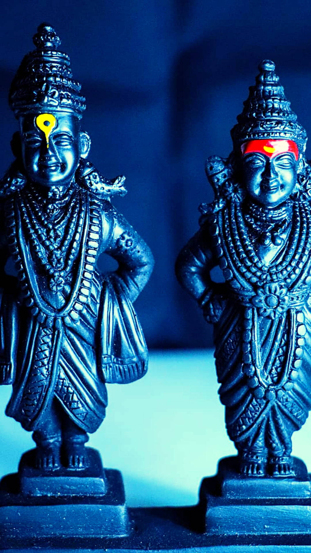 Lord Shiva 桌布 壁紙 — 兩尊華麗的印度教神像，帶有複雜的珠寶和發光的額頭標記，站在冷藍色燈光下。