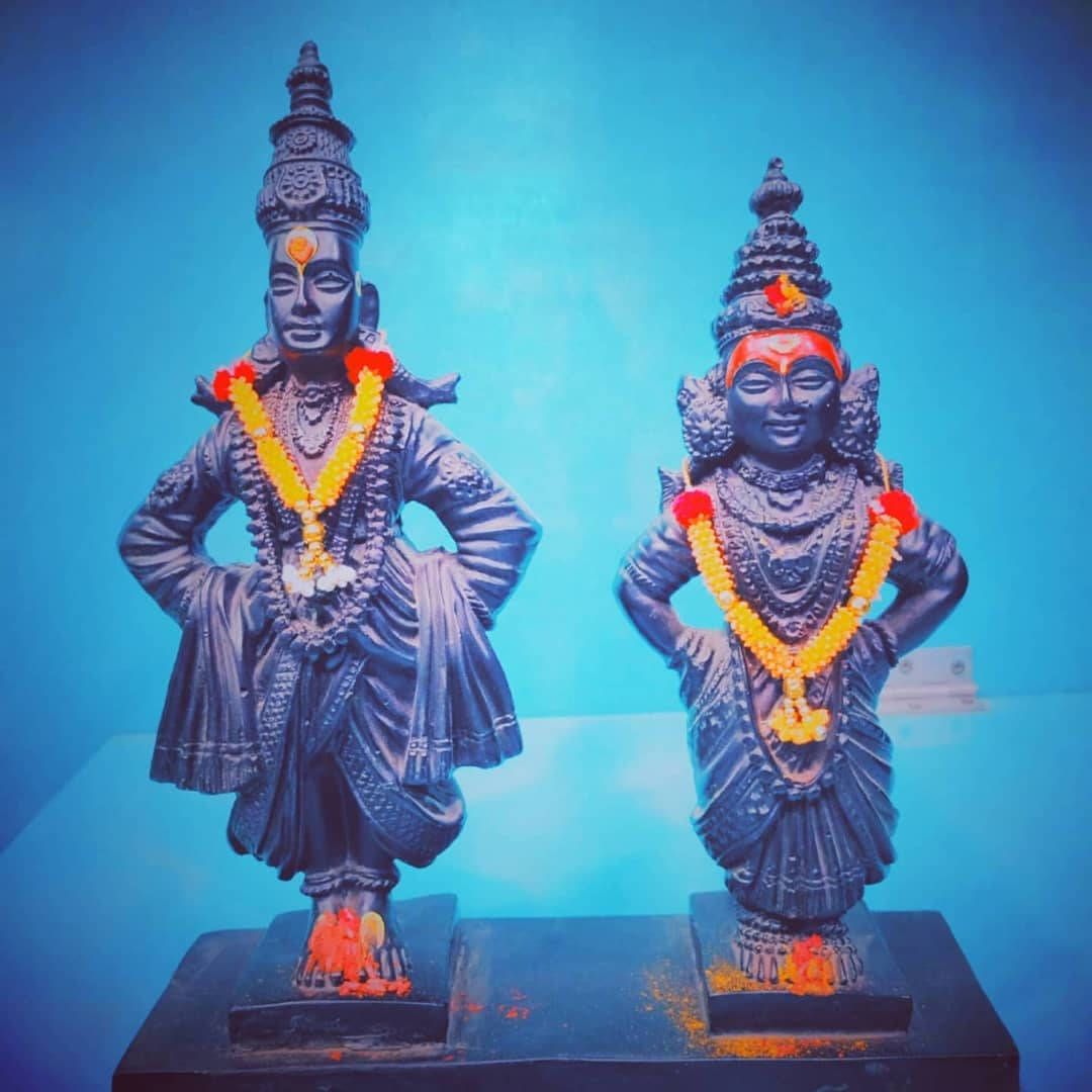 Statue Aesthetic 桌布 壁紙 — 兩尊華麗的深色雕像飾以鮮豔的黃色和紅色花環，並排站立在鮮明的藍色背景前。