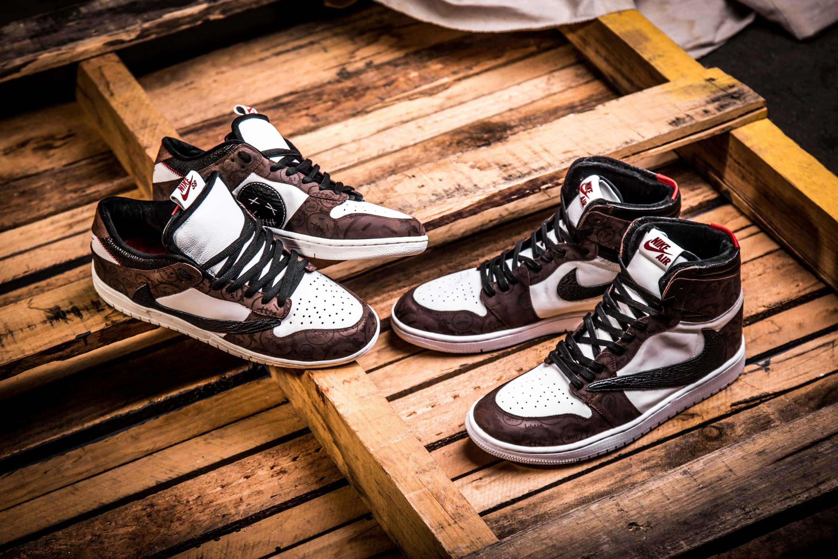 Travis Scott Jordan 1 桌布 壁紙 — 兩對棕色和白色的高筒運動鞋，搭配黑色鞋帶，放在一個風化的木托盤上。