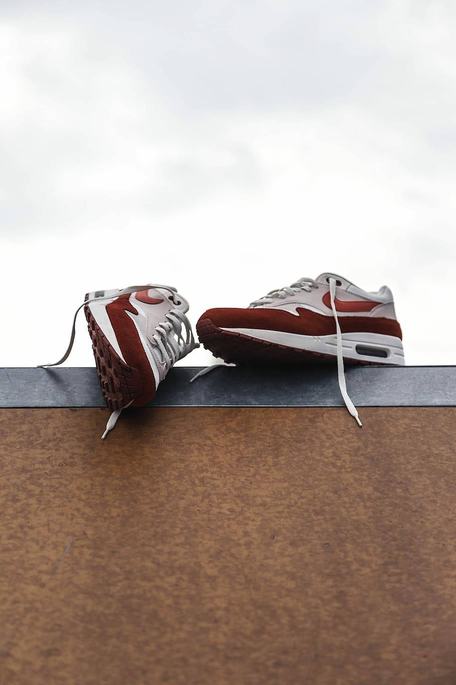 Nike Air Max 1 OG Ultra Red 壁紙 — 兩對紅白波鞋隨意地放在生鏽的金屬架上，背景是陰天。