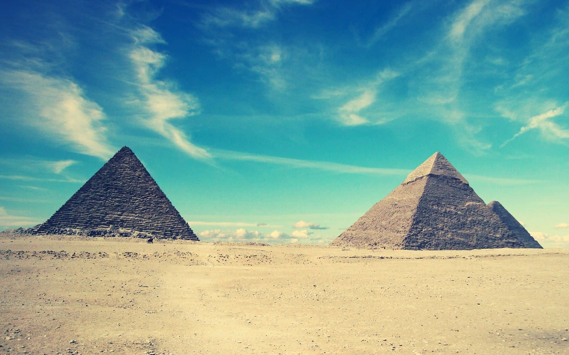 Egypt 桌布 壁紙 — 兩座古老金字塔在金色沙漠中雄偉地聳立，上方是帶有縷縷輕雲的鮮豔藍天。
