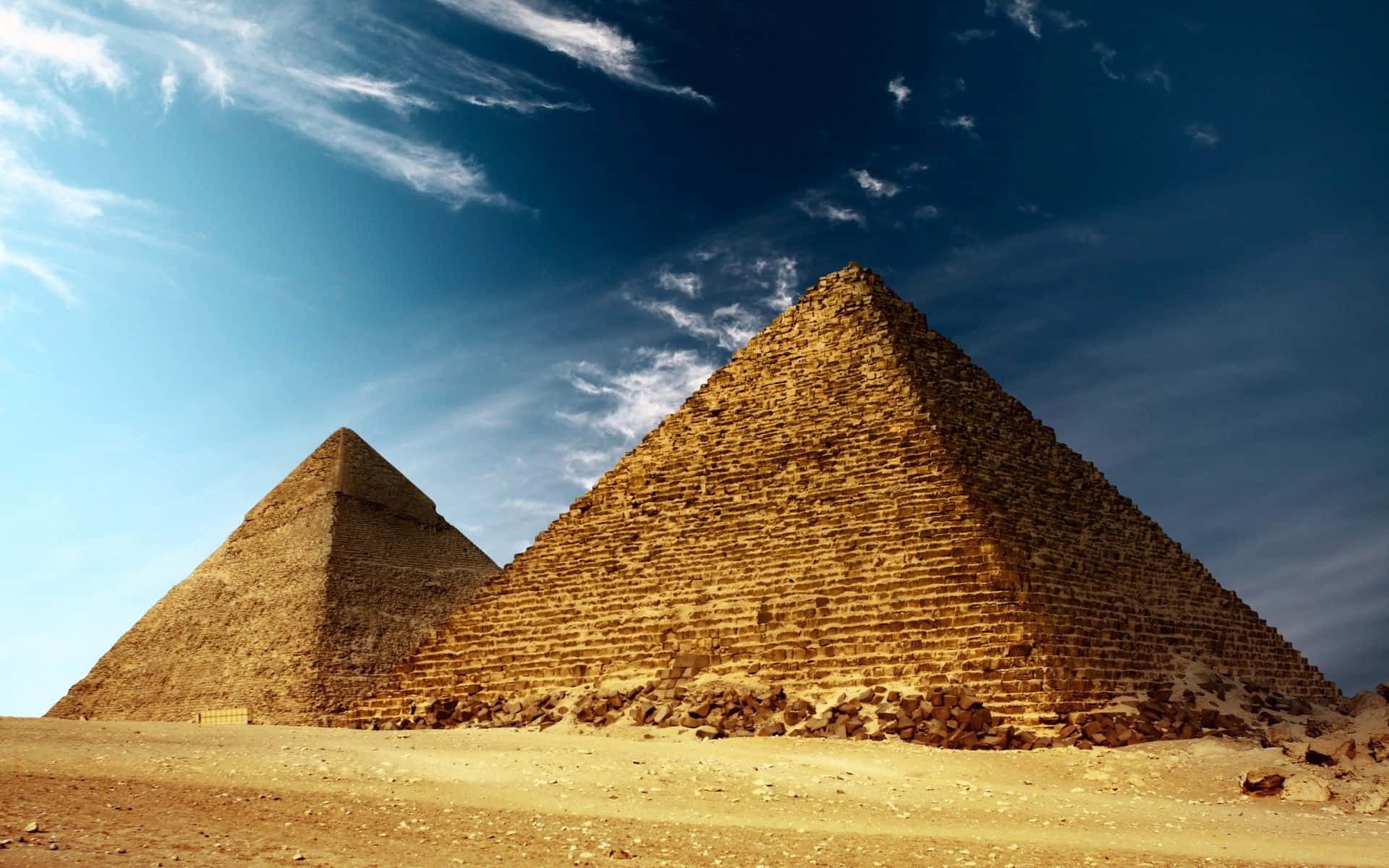 Egypt 桌布 壁紙 — 兩座巨大的古老金字塔從金色沙漠中升起，在蔚藍的天空下，天空中有縷縷薄雲。