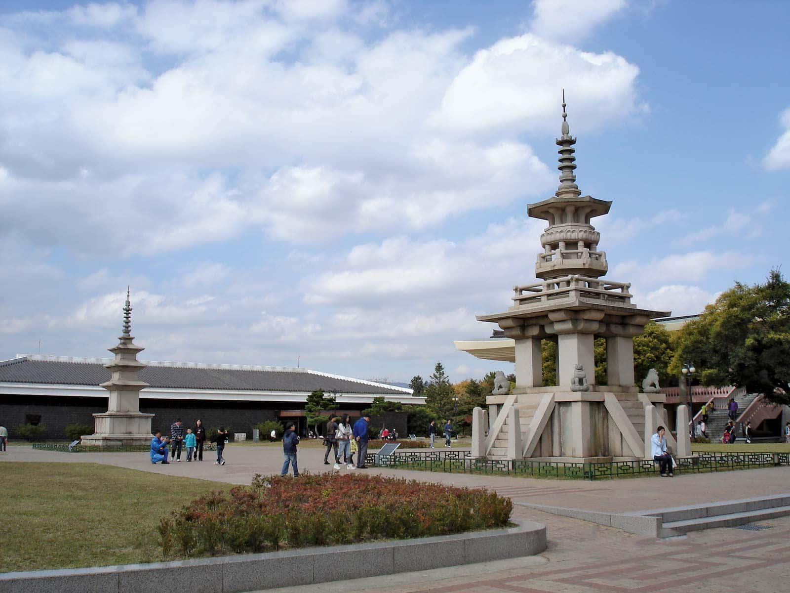 South Korea 桌布 壁紙 — 兩座石塔喺公園入面高高聳立，天空局部多雲，有遊客喺度漫步。
