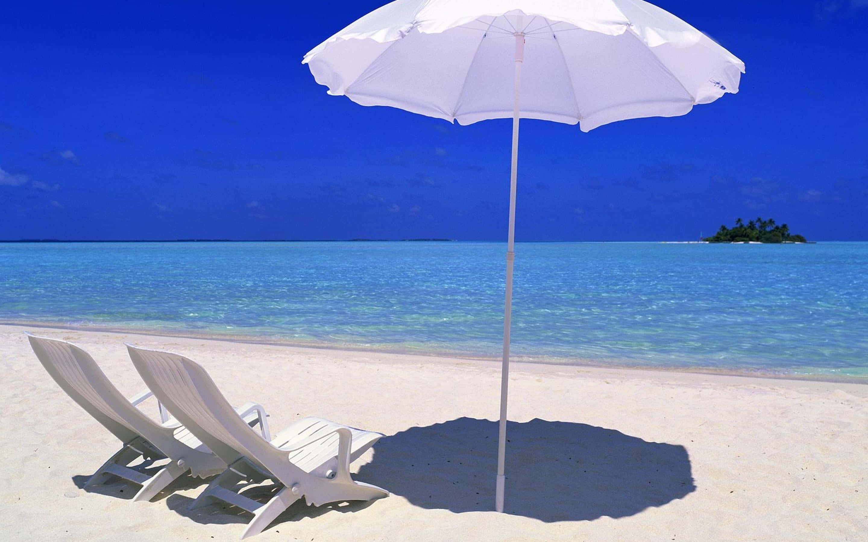 Beach Sunbed 桌布 壁紙 — 兩張白色躺椅放在白色遮陽傘下，位於純淨沙灘上，面向碧綠海水和遠處的熱帶島嶼。