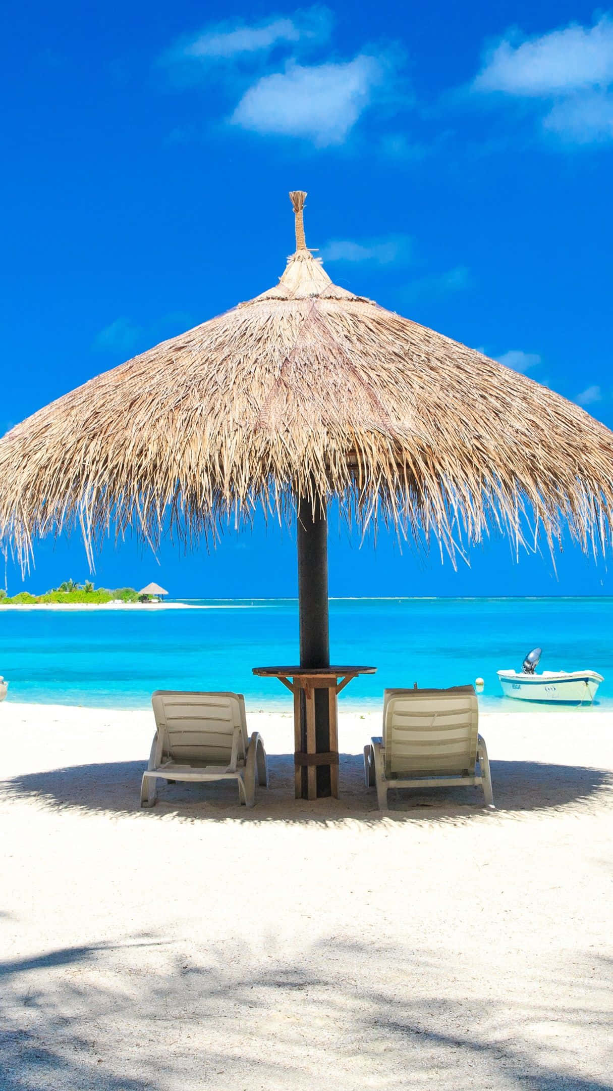 Beach Sunbed 桌布 壁紙 — 兩張躺椅放在茅草傘下，位於純淨白沙灘上，遠處有碧綠海水和小船。