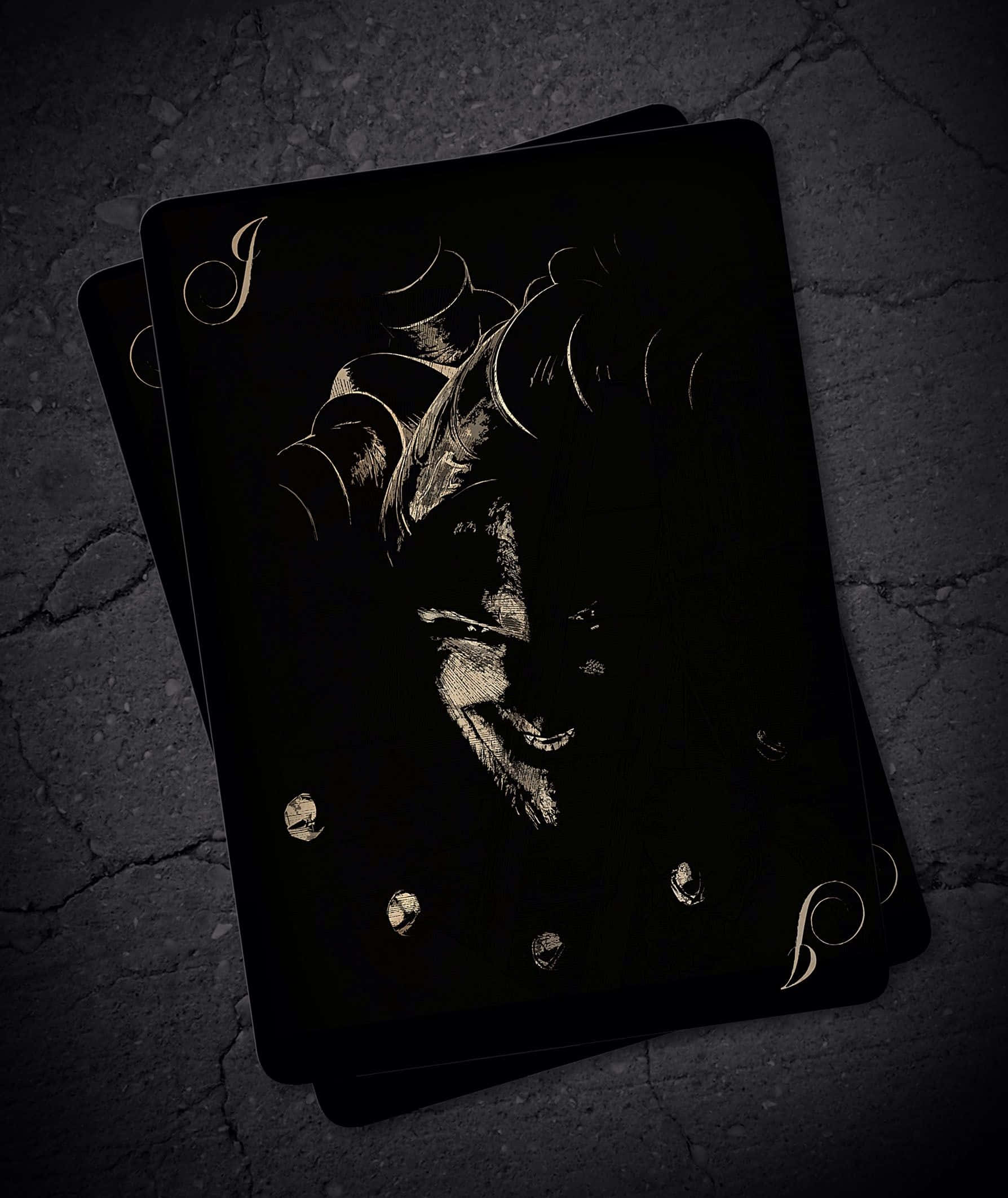 Joker Card 桌布 壁紙 — 兩張黑色啤牌帶有金色積克插圖，在昏暗燈光下放置於裂開的混凝土上。