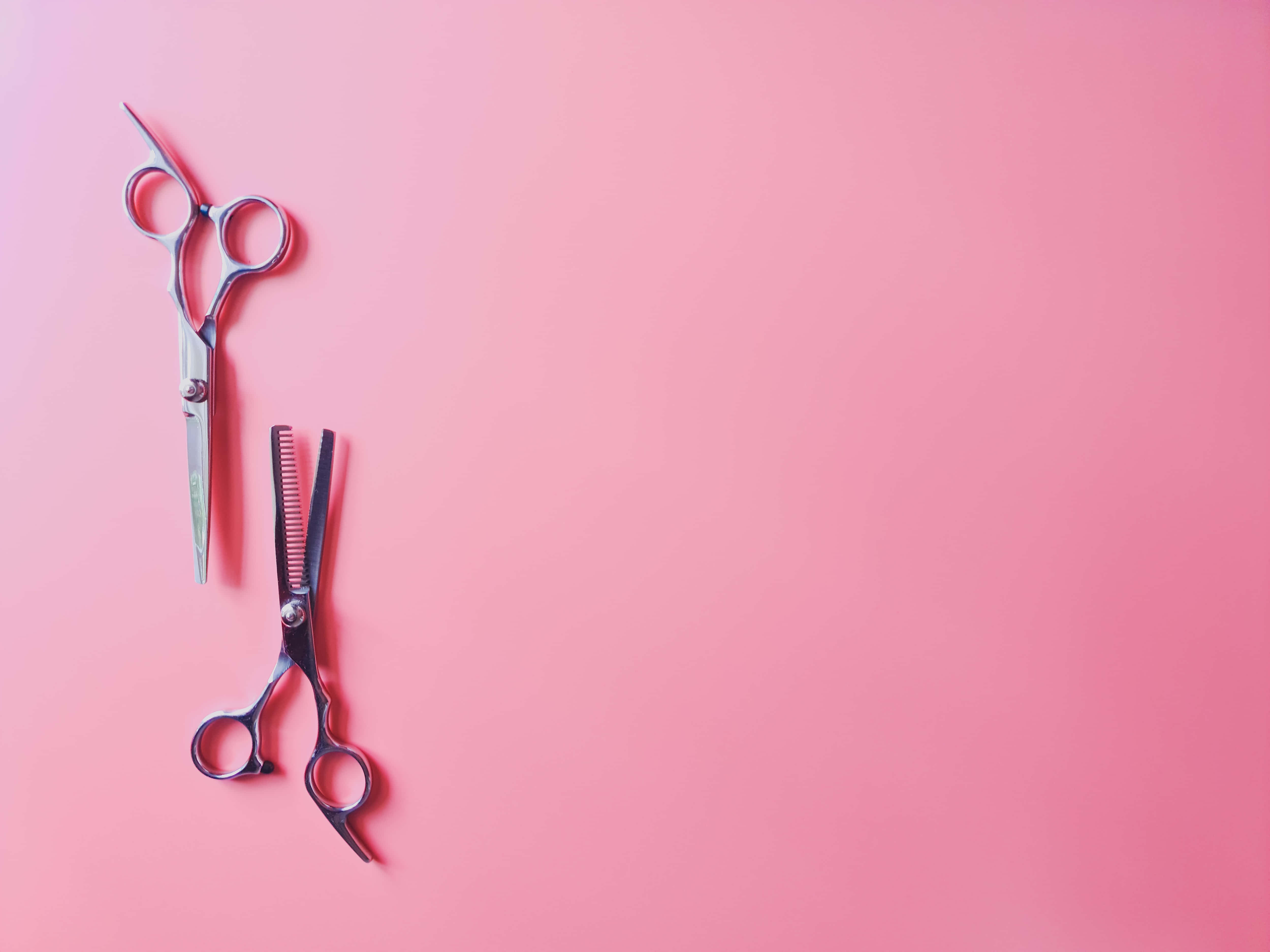 Haircare 桌布 壁紙 — 兩把專業理髮剪刀和一把梳子放在純粉紅色背景上，呈現極簡的平鋪佈局。
