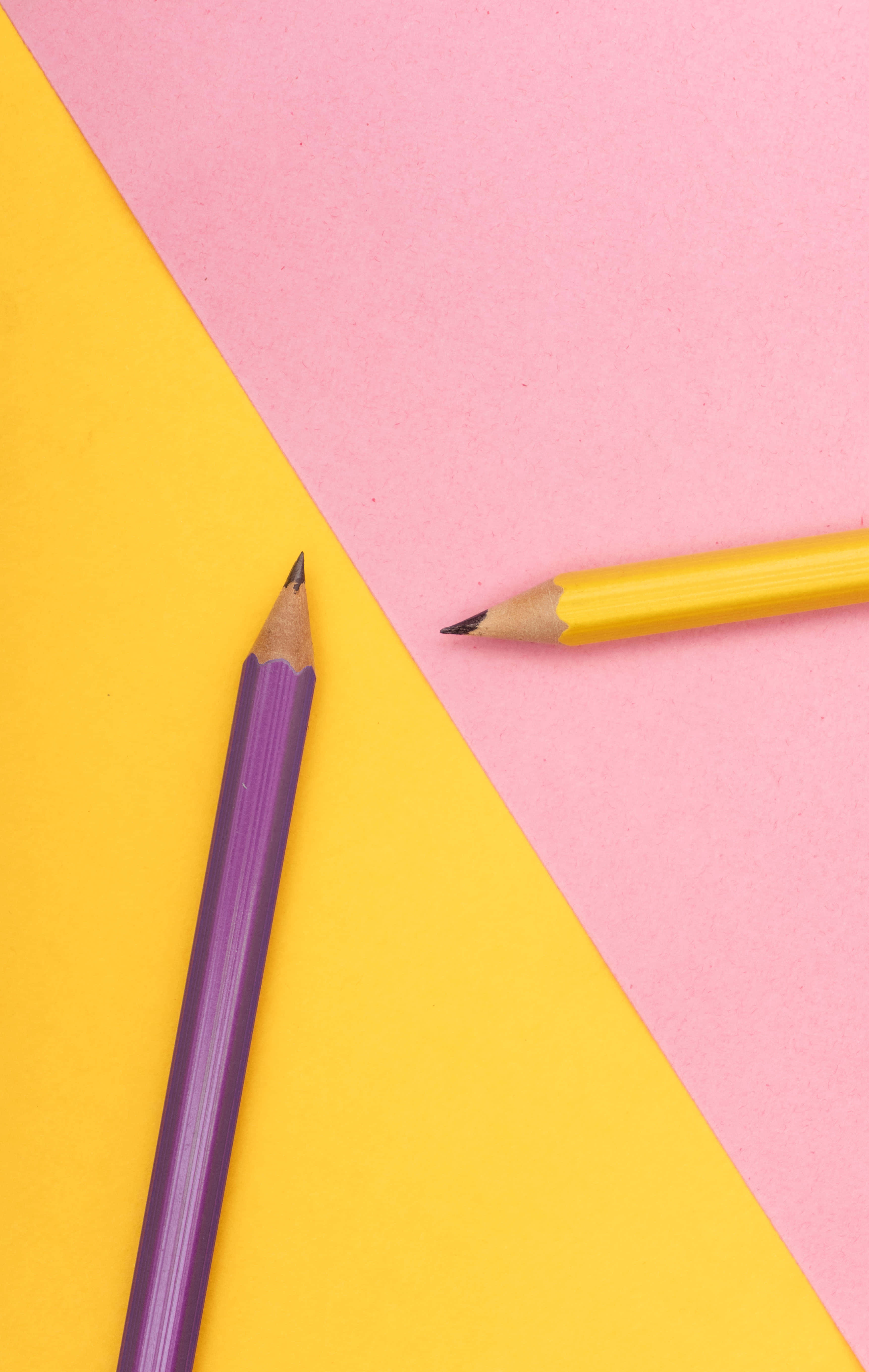 pencil 桌布 壁紙 — 兩支削尖的顏色筆斜放在充滿活力的黃色和粉紅色幾何背景上。