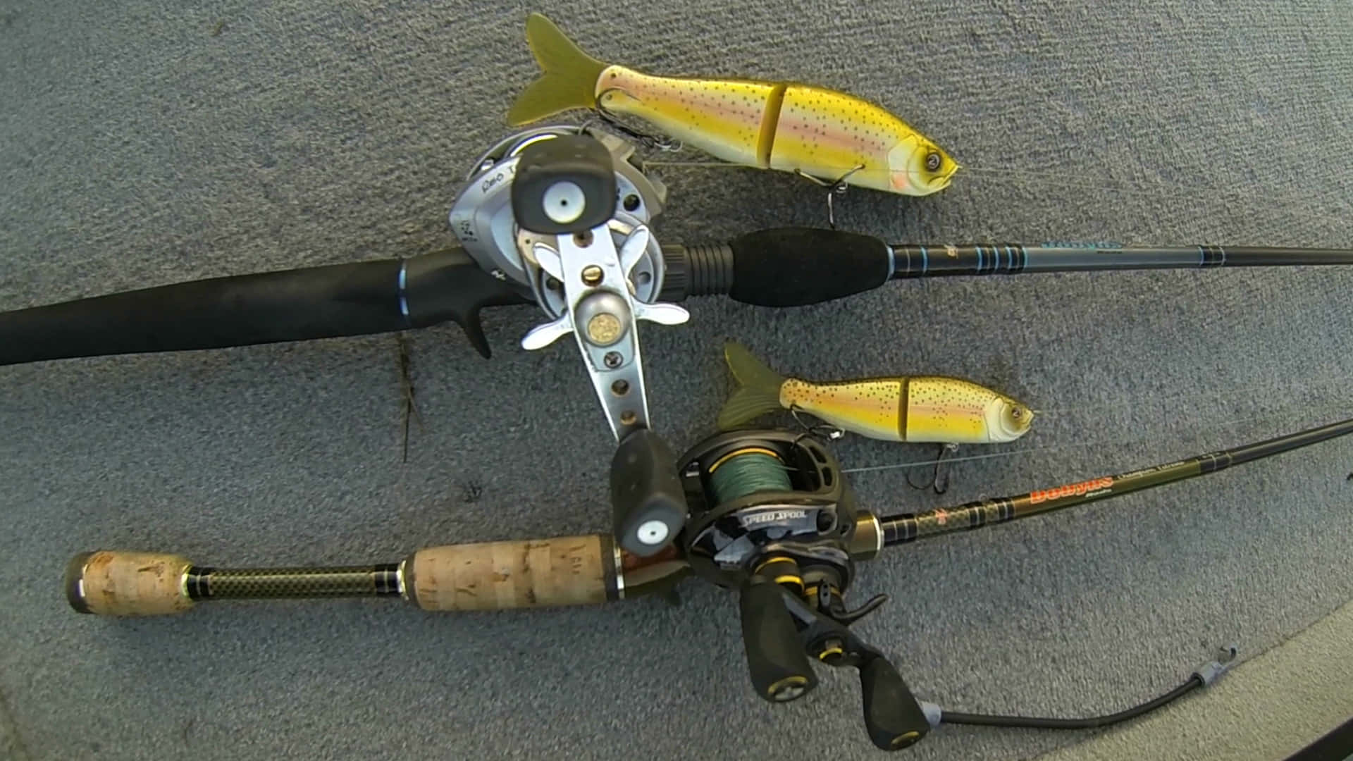 Fishing Bait 桌布 壁紙 — 兩支帶有捲線器和黃色鱒魚假餌的釣魚竿放在灰色地毯上。
