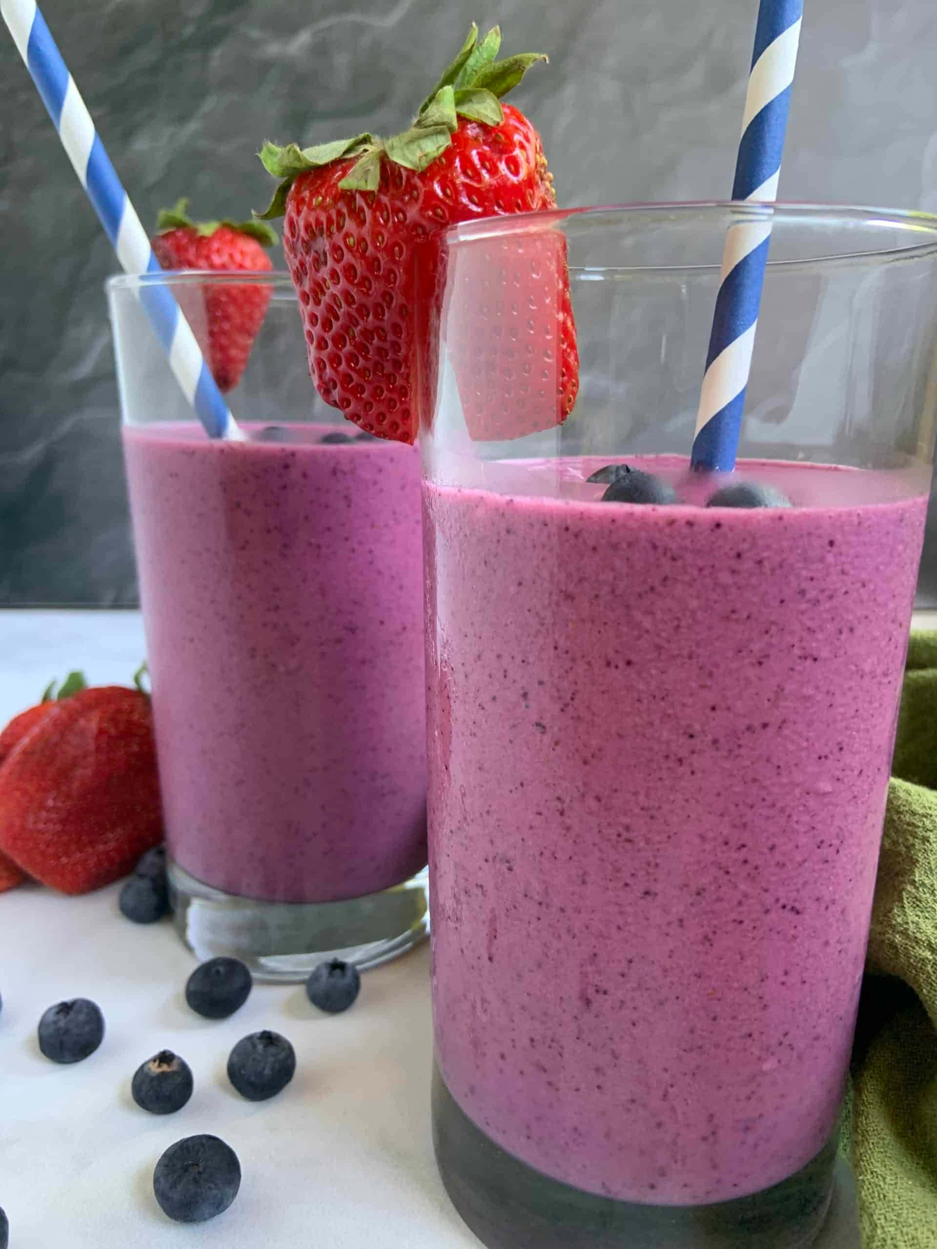 Blueberry Smoothie 桌布 壁紙 — 兩杯充滿活力的紫色冰沙，配上新鮮草莓和藍莓，並插上條紋吸管。