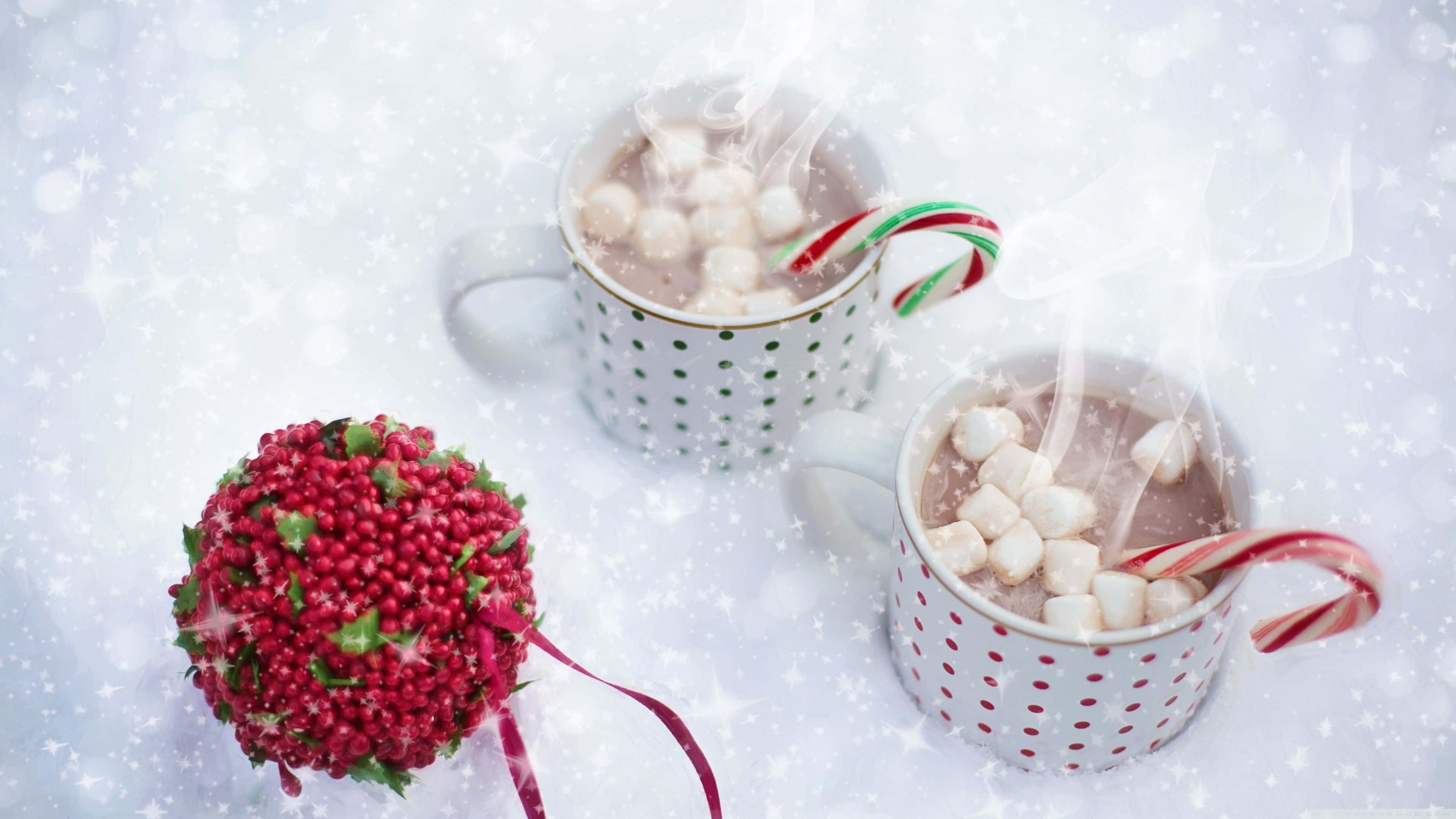 Winter Food 桌布 壁紙 — 兩杯冒著熱氣的熱朱古力，上面有棉花糖和拐杖糖，放在飄雪中一個紅色石榴裝飾旁邊。