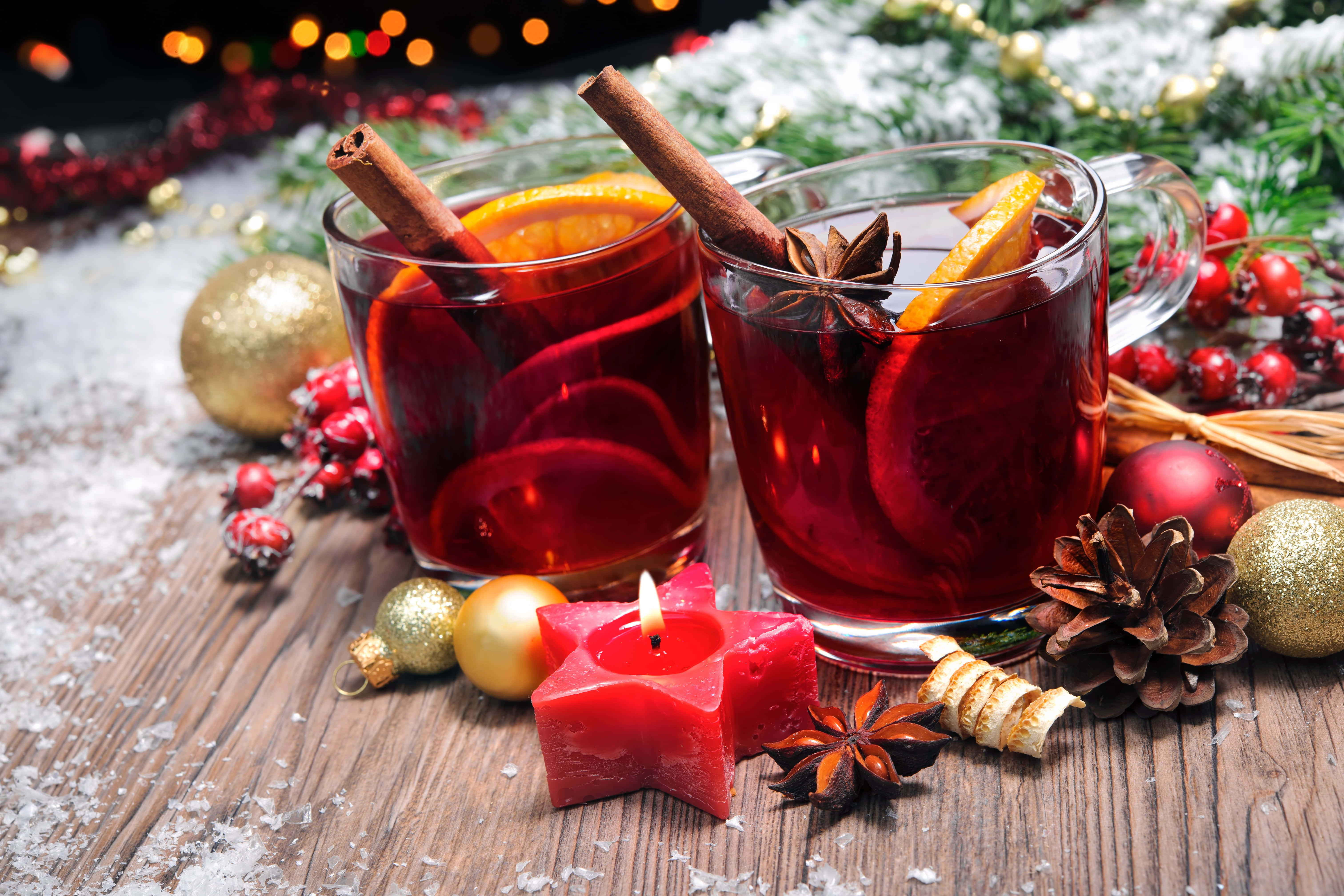 Mulled Wine 桌布 壁紙 — 兩杯冒著熱氣的香料熱紅酒，配以肉桂棒和橙片，放在鋪滿雪的木桌上，旁邊有節日裝飾和點燃的星星蠟燭。