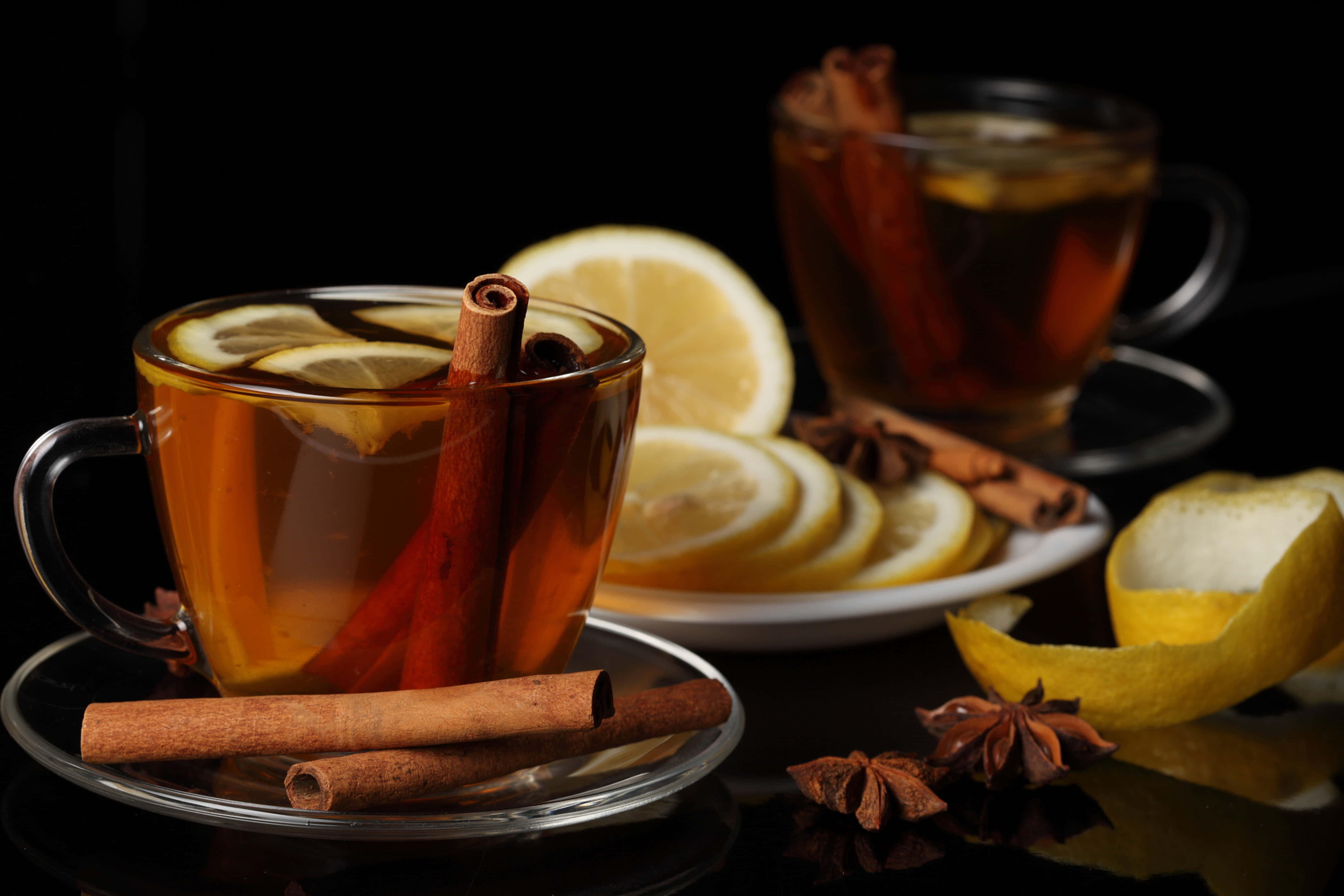 Mulled Wine 桌布 壁紙 — 兩杯冒著熱氣的香料茶，配上檸檬片和肉桂棒，在深色背景下溫暖地發光。