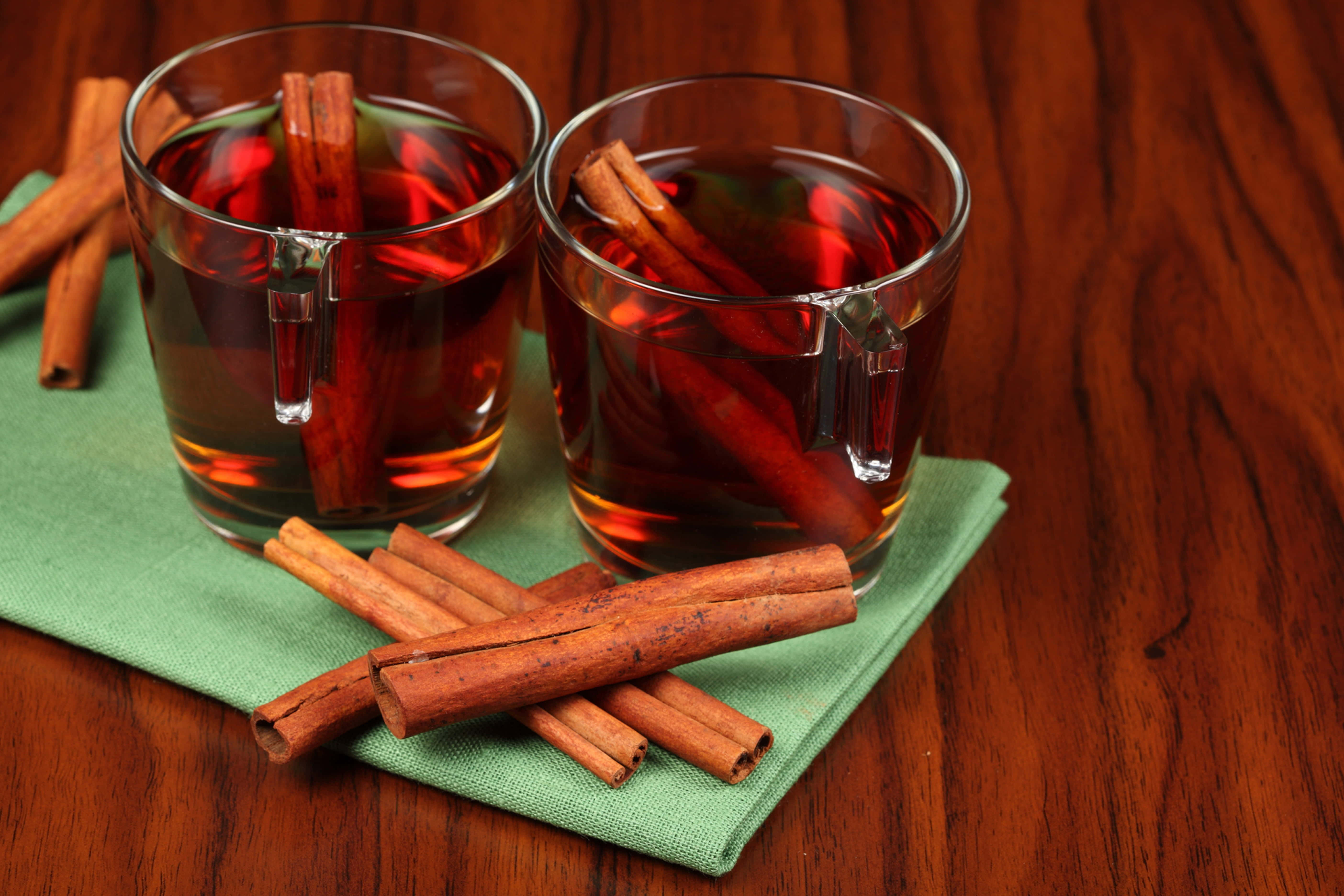 Mulled Wine 桌布 壁紙 — 兩杯加了肉桂棒的香料蘋果酒放在溫暖木桌上的綠色餐巾上。