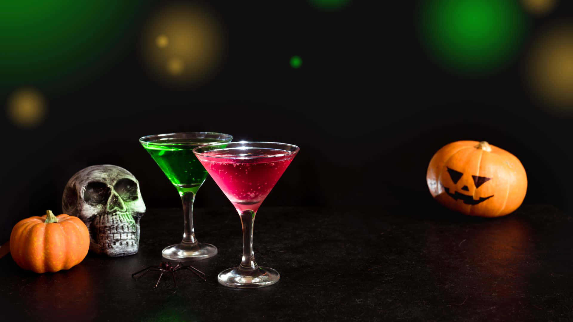 Spooky Cocktails 桌布 壁紙 — 兩杯發光的馬提尼雞尾酒放在南瓜和骷髏旁邊，置於帶有綠色散景燈光的暗色桌子上。