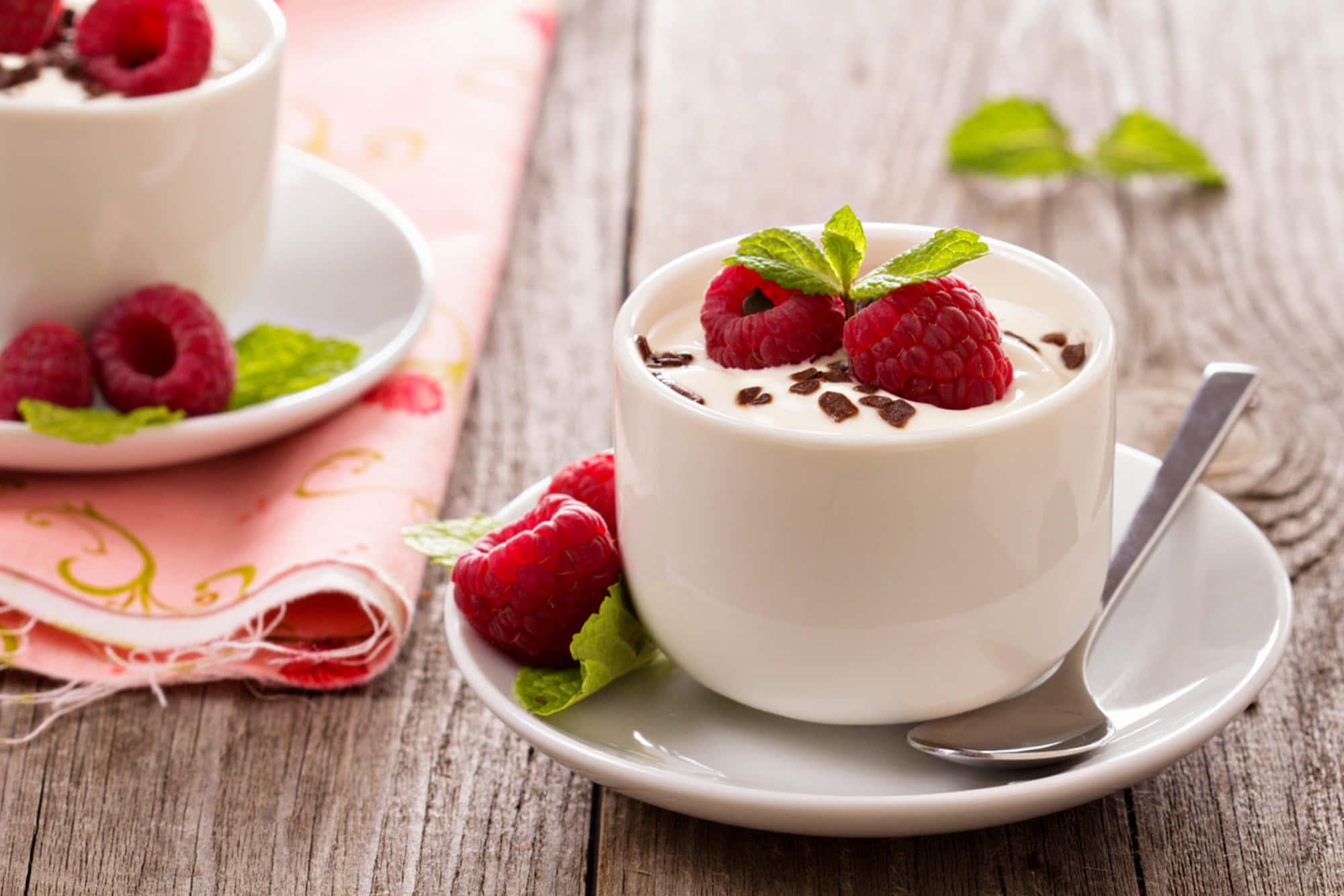 Cute Dessert 桌布 壁紙 — 兩杯白色奶油甜品，上面鋪上新鮮覆盆子、薄荷葉和朱古力碎，放在質樸的木桌上。