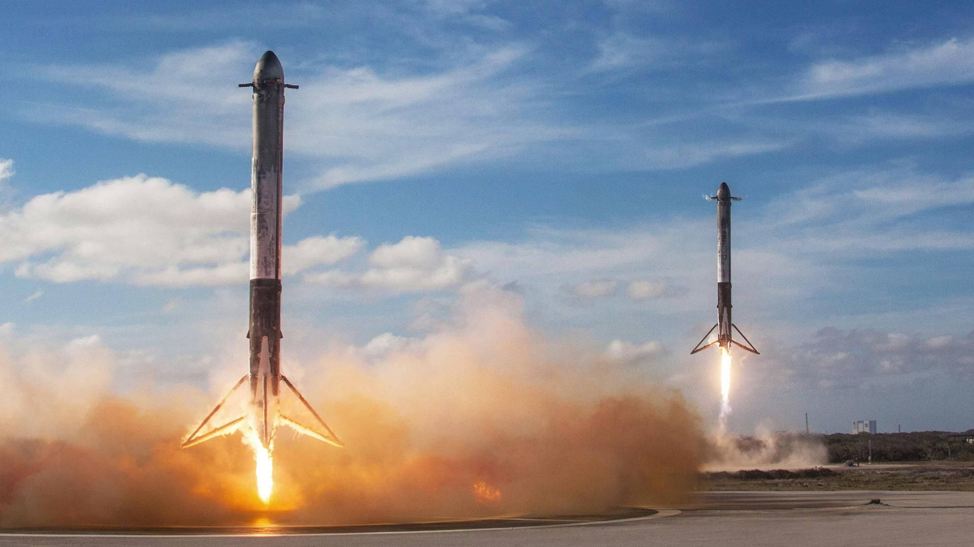 兩枚火箭在藍天下發射，伴隨著明亮的火焰和煙霧。 — Spacex GIF 壁紙